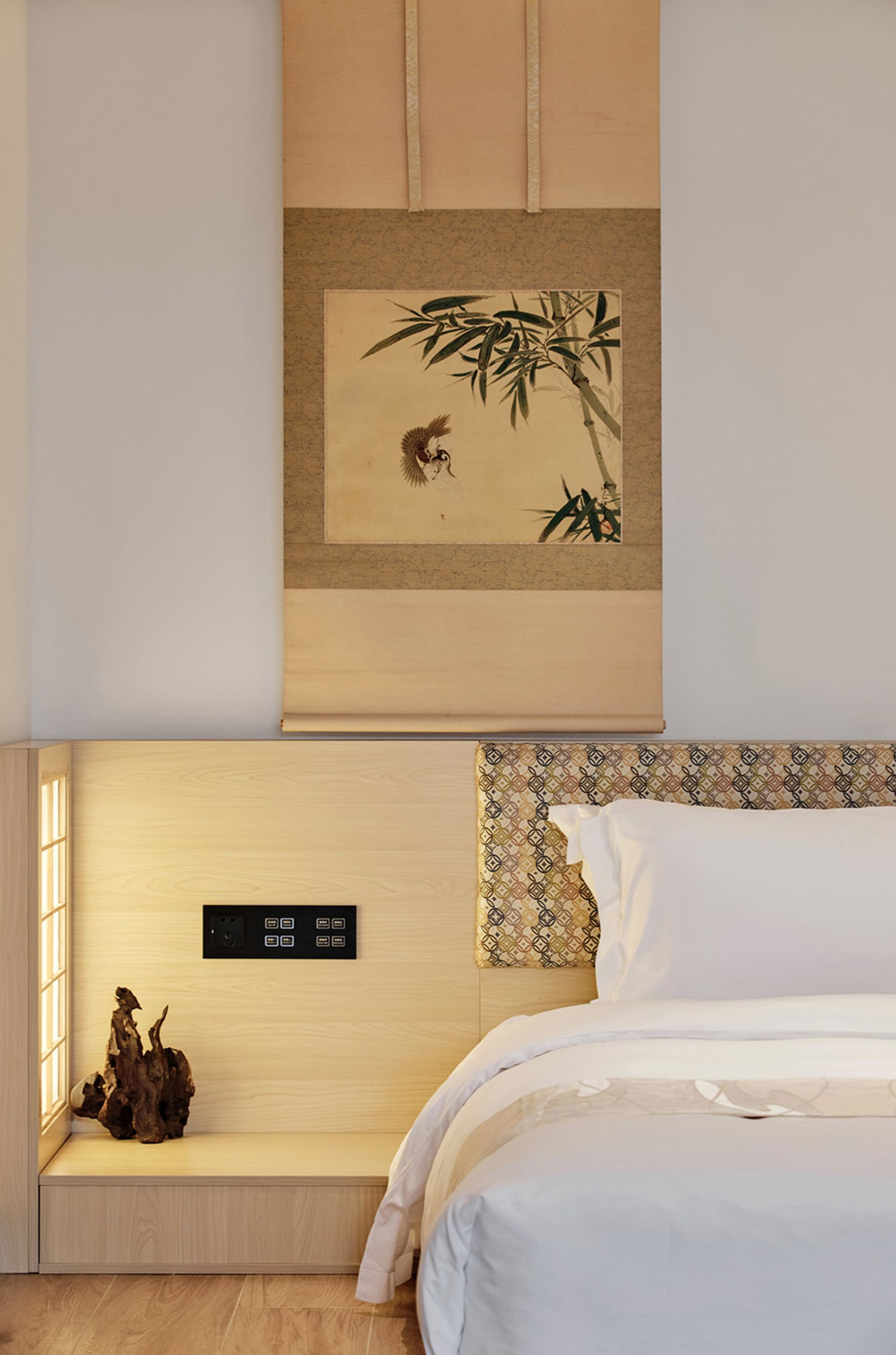 A minimalist bedroom with a wooden headboard, white bedding, and a framed painting above the bed.