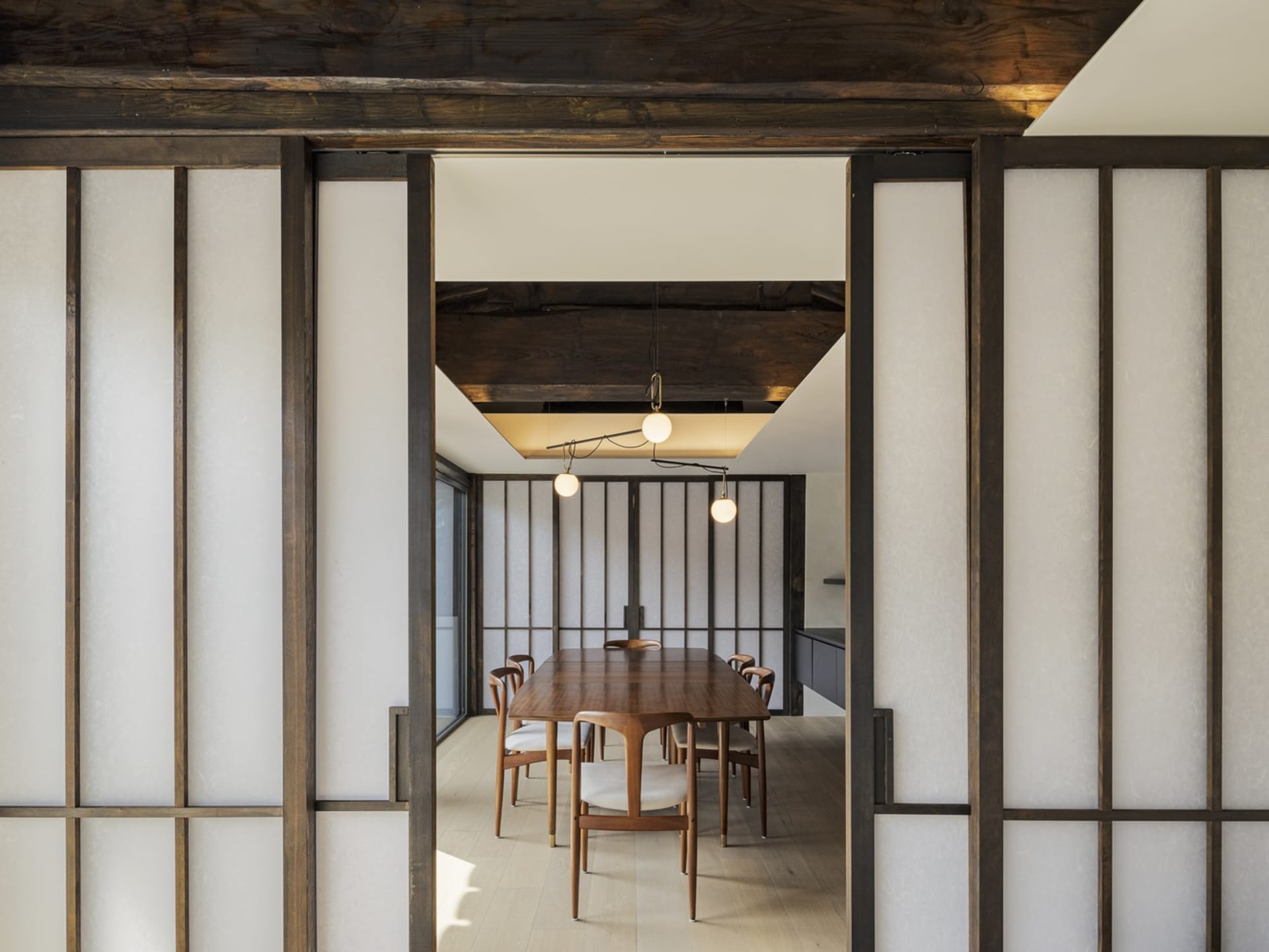 一間現代餐廳，設有木質推拉門及木製餐桌，餐桌周圍環繞著餐椅，空間呈現簡約風格
