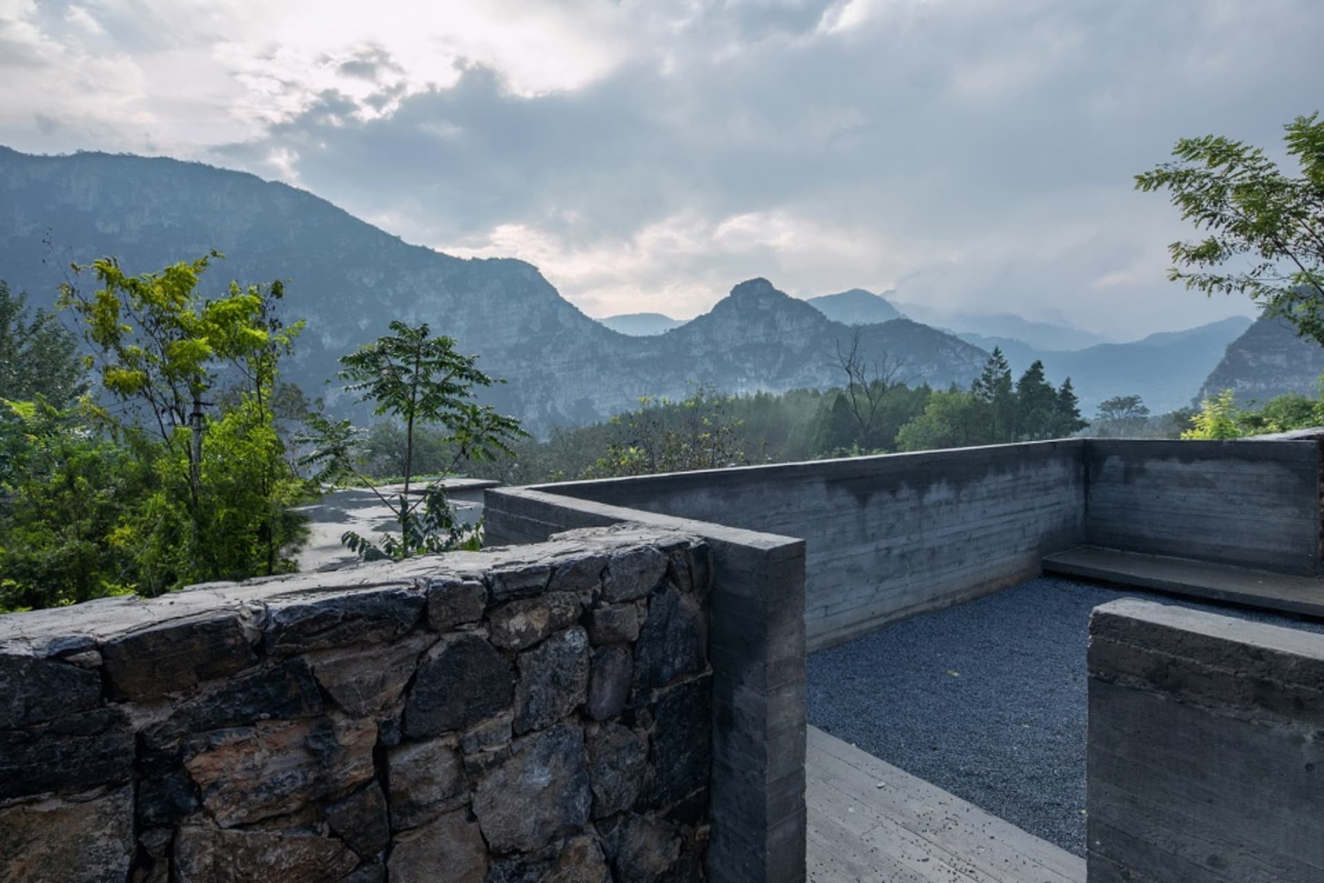 A scenic outdoor view with hills and mountains in the distance, featuring natural construction elements like stone and concre