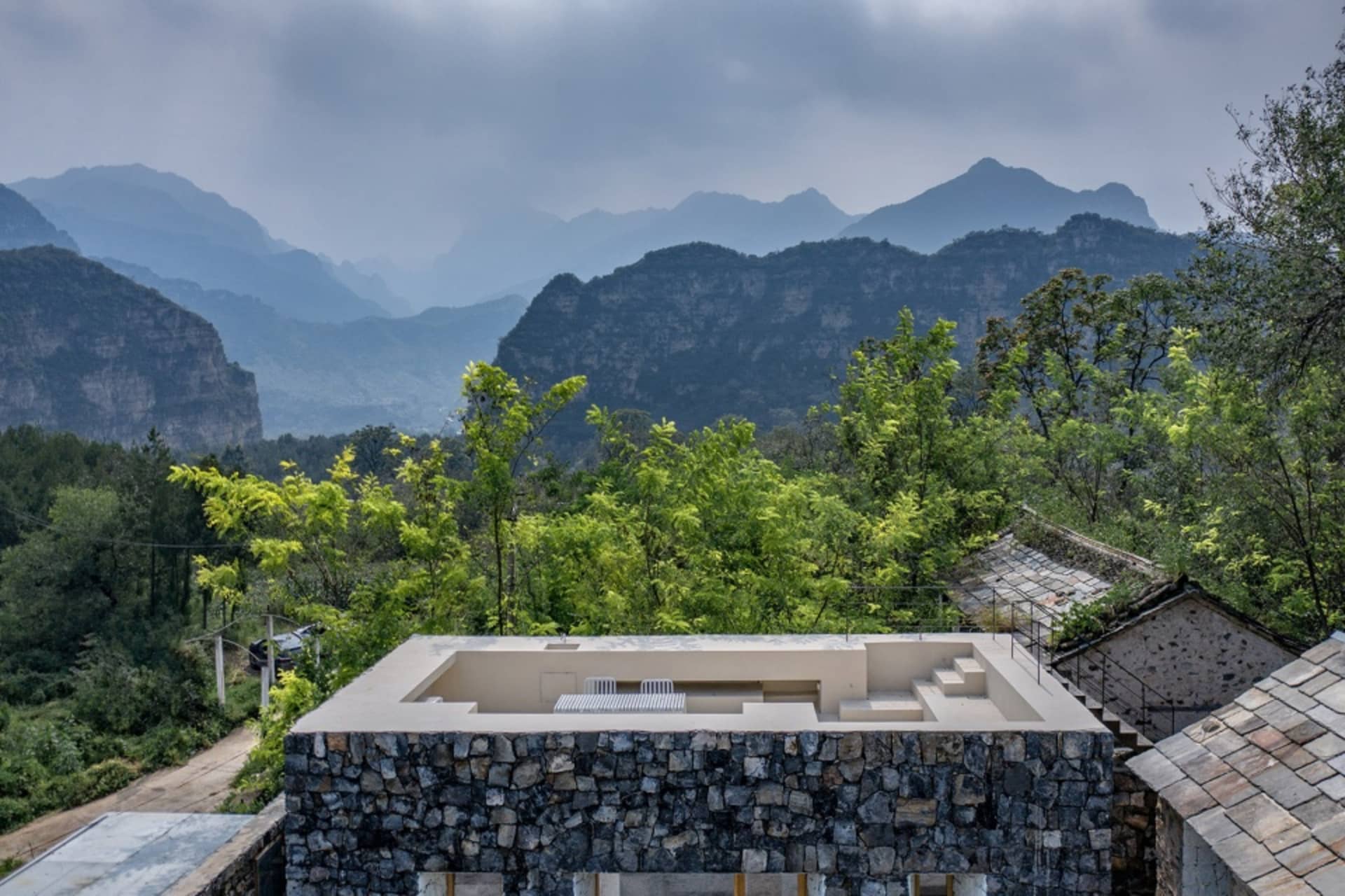 A stone-walled residence set against a backdrop of lush green mountains and dense foliage.