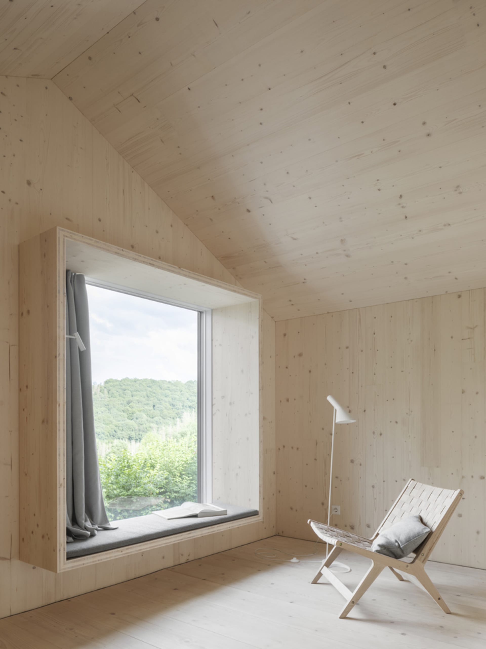 A minimalist room with a window seat, white walls, and a floor lamp facing a wooden chair.