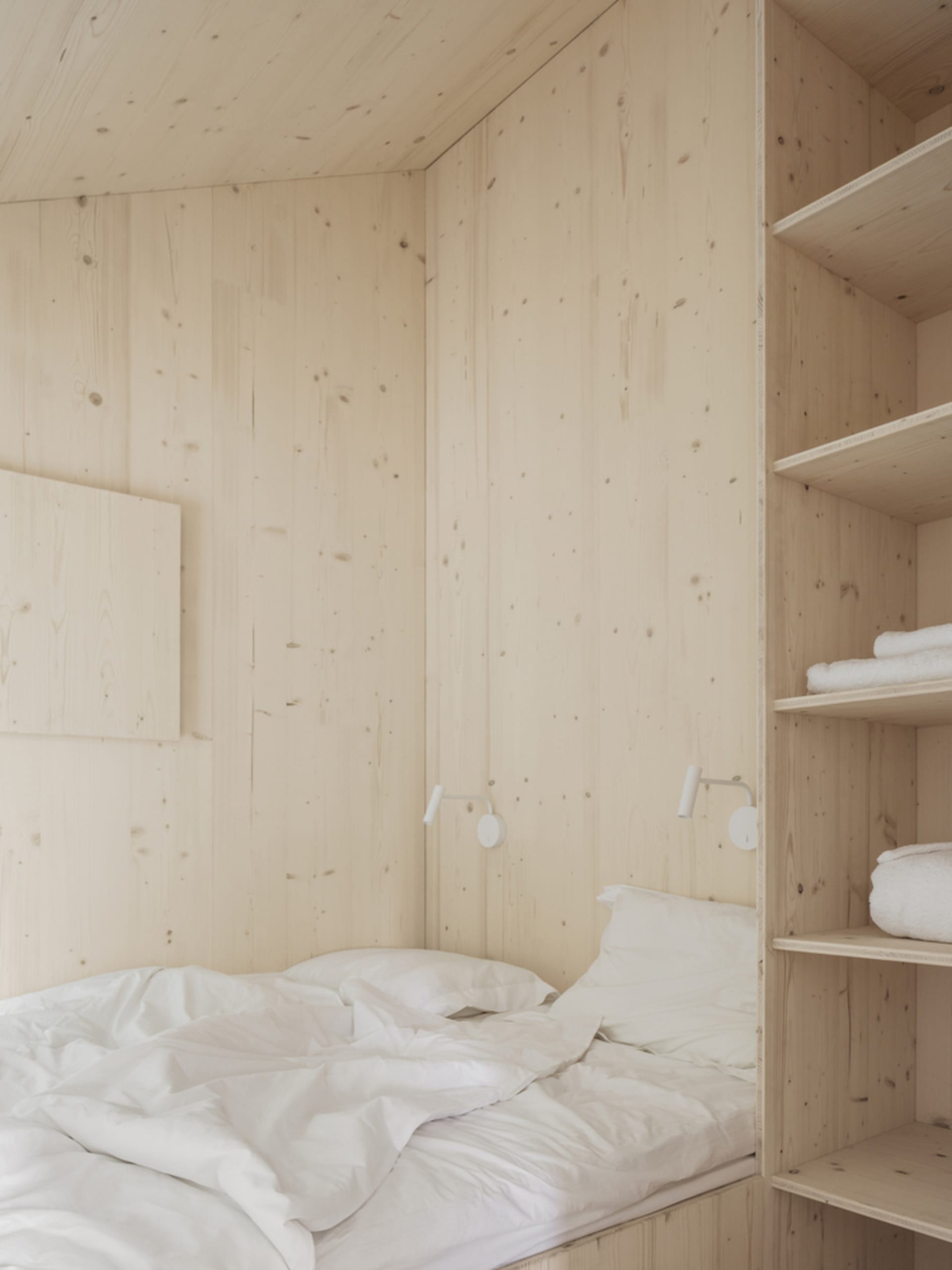 A minimalist bedroom with white wood walls and a bed with white bedding.
