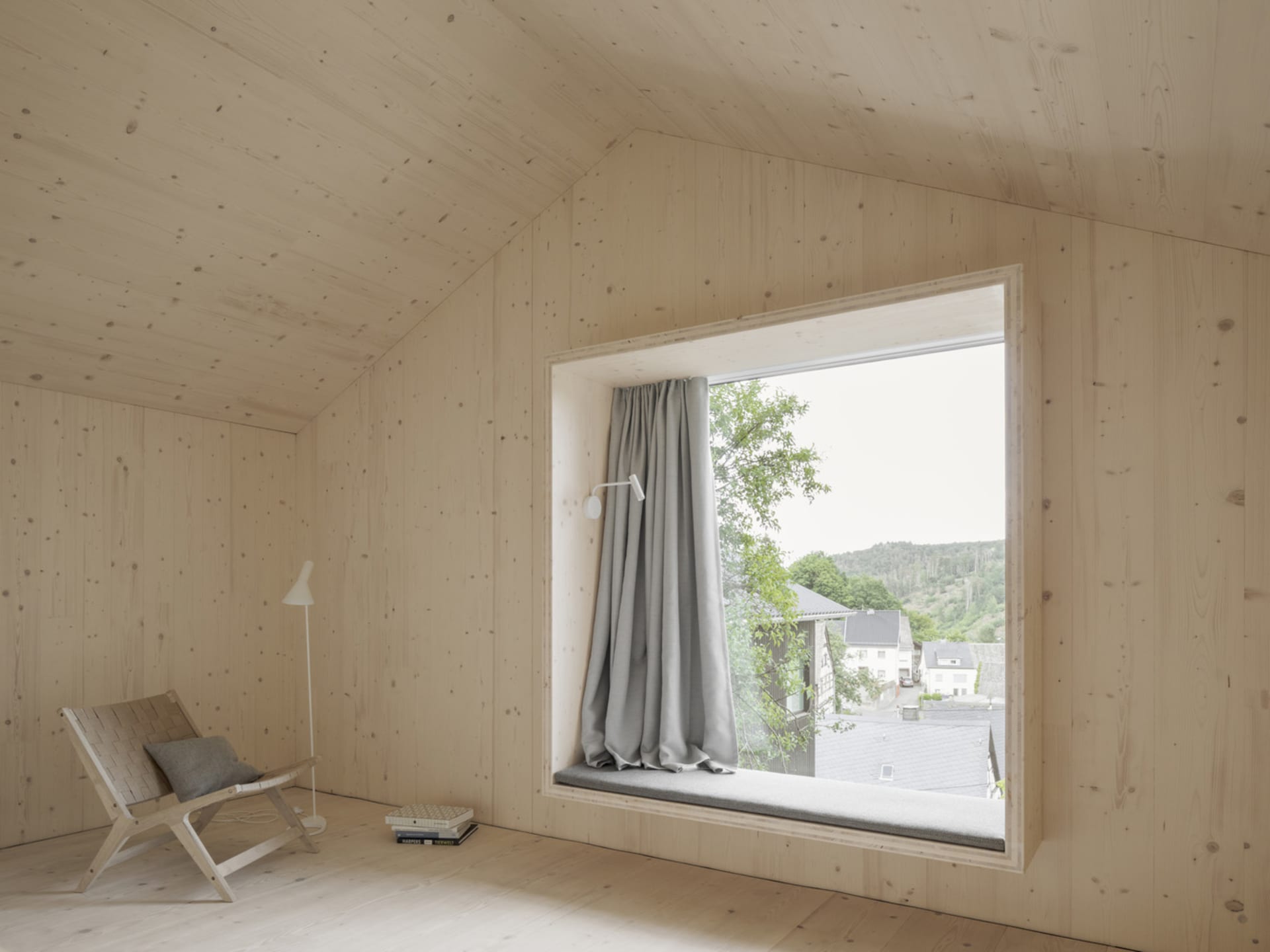 A minimalist window seat made of wood with a cushion and a gray curtain.