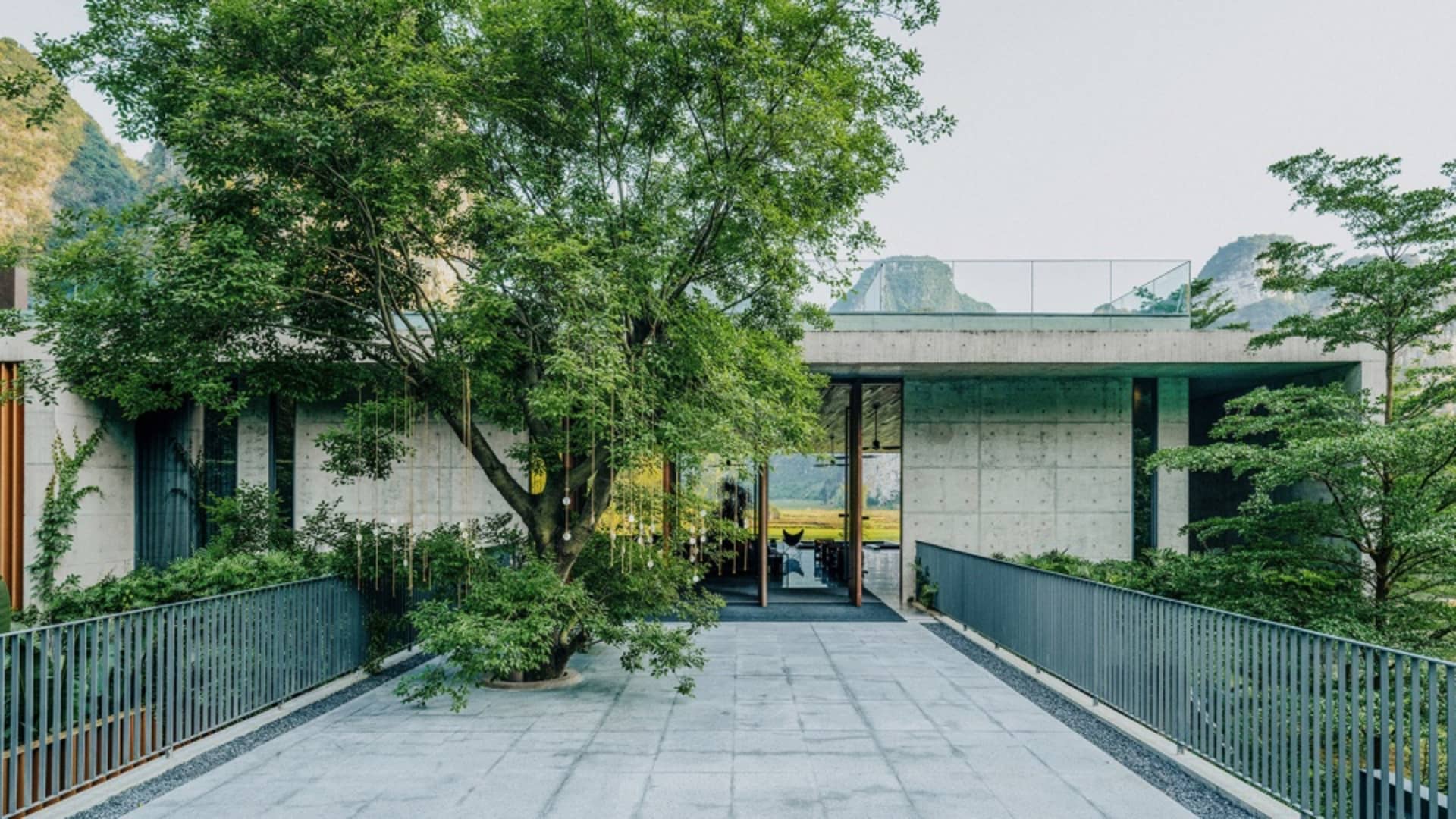 一座現代建築，擁有混凝土外牆與玻璃元素，周圍環繞綠樹與山景。