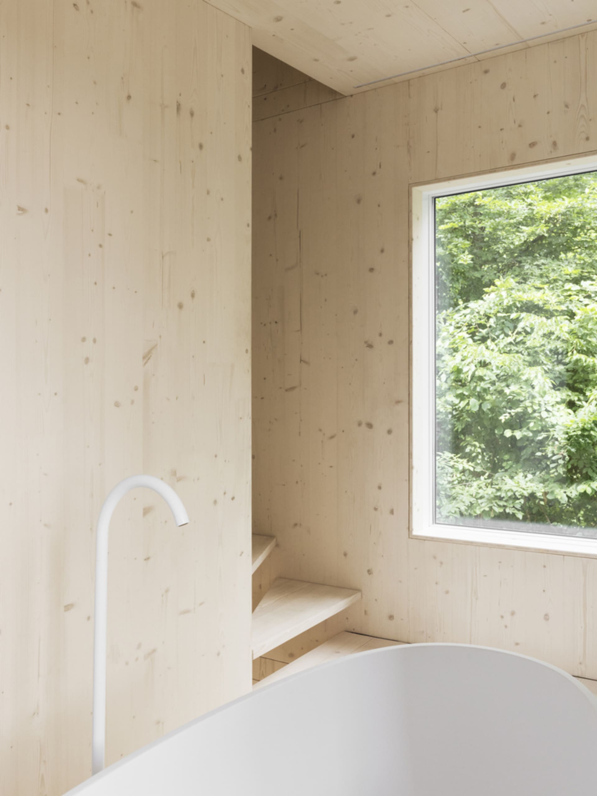 Modern minimalist bathroom featuring wood-paneled walls, a white bathtub, and a set of stairs.
