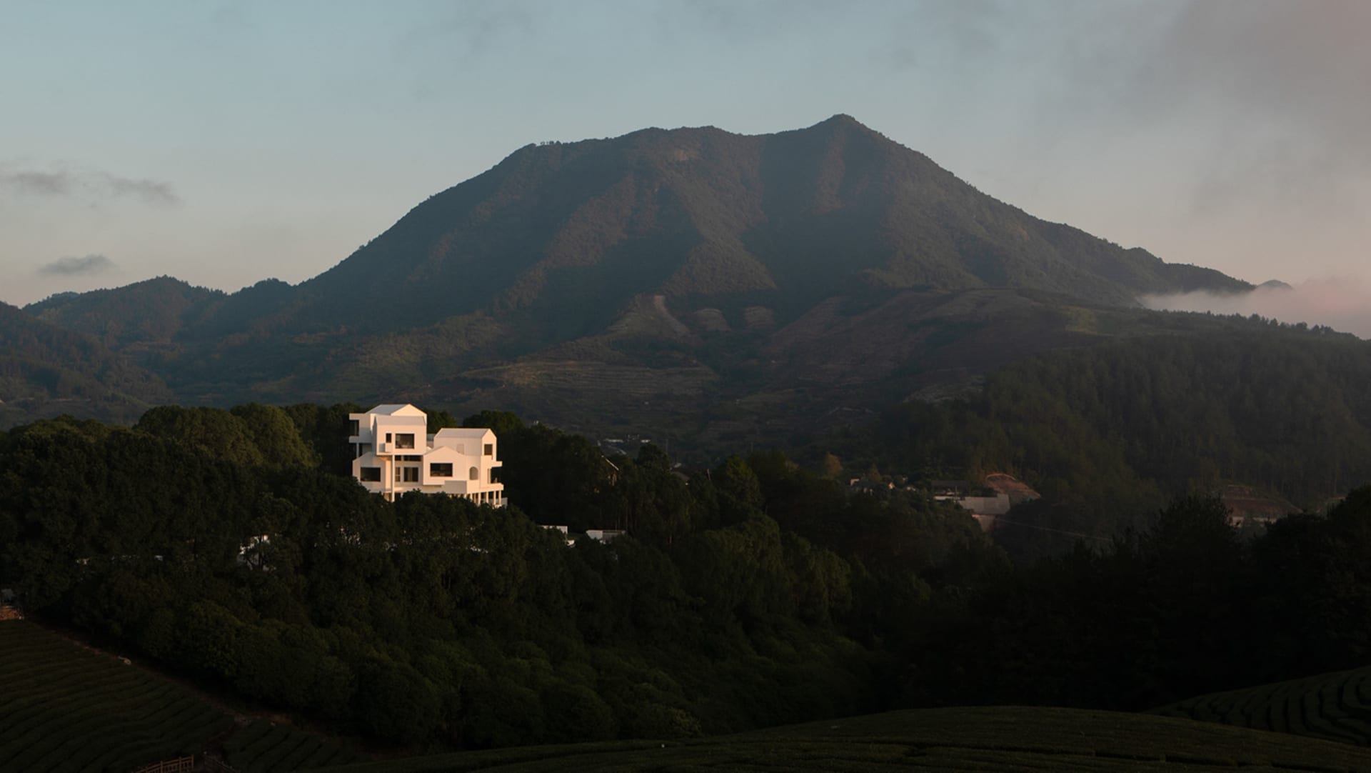 A serene mountain landscape with a prominent white building in the foreground, surrounded by lush greenery and rolling hills.