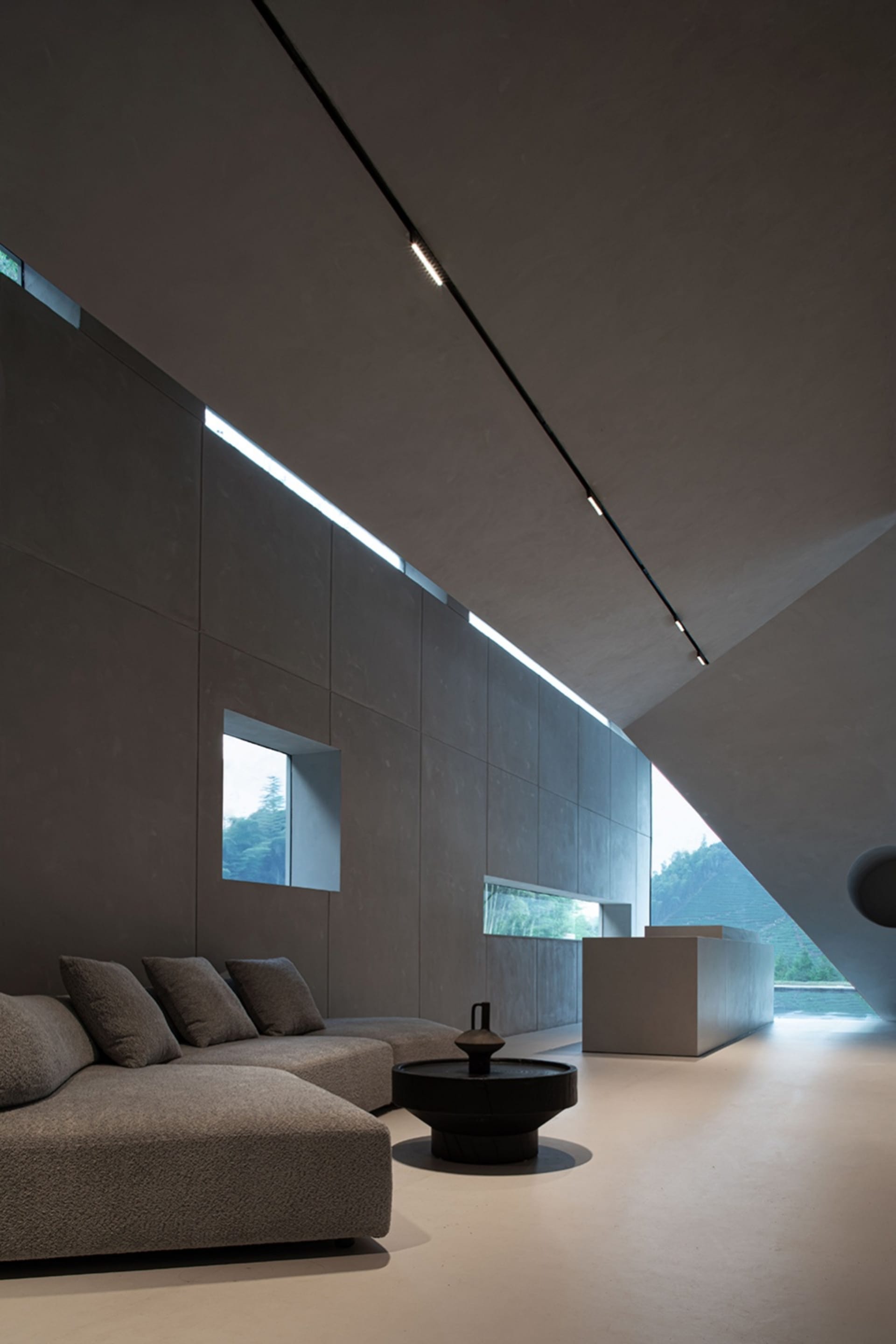 Modern living room with concrete and glass walls, featuring a contemporary sofa and minimalist decor.