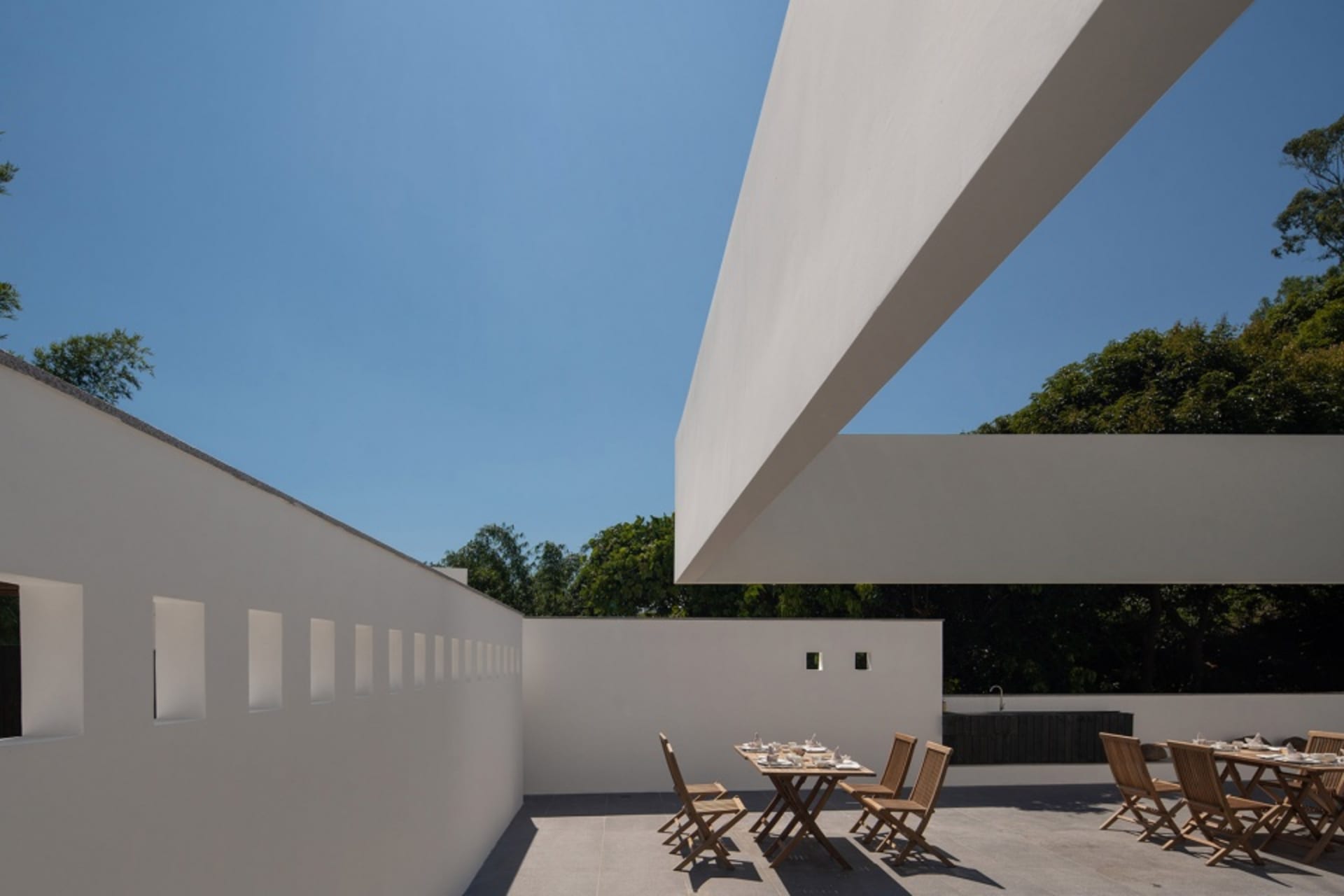 Modern patio with concrete walls, glass walls, and a table setting.