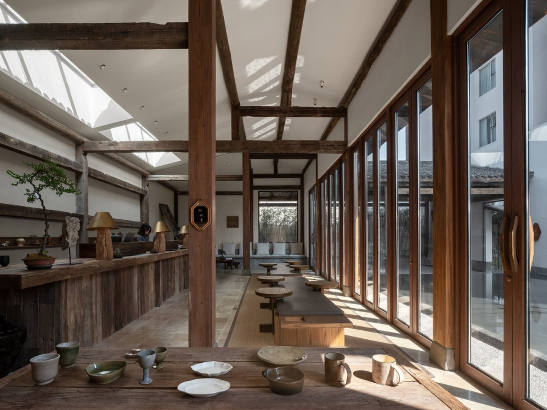 A spacious, modern restaurant interior featuring a wooden counter, chairs, and various tableware items on a counter.