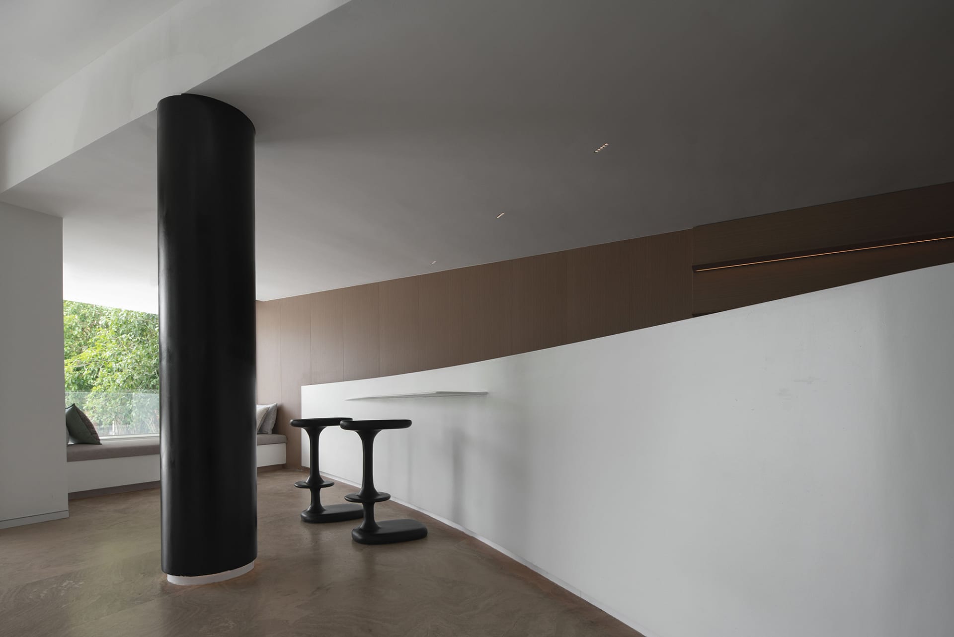 Minimalist interior with concrete barstools and a large black column.