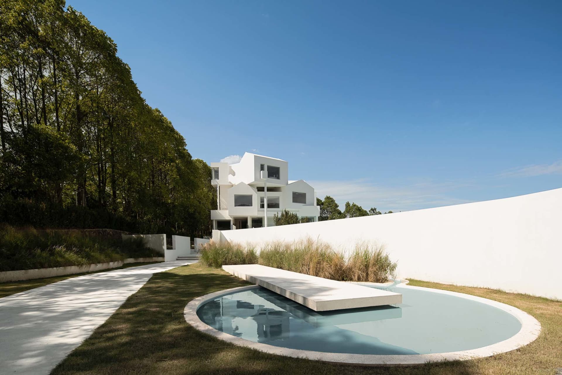A modern, minimalist residential home with white architectural elements surrounded by greenery on a clear day.