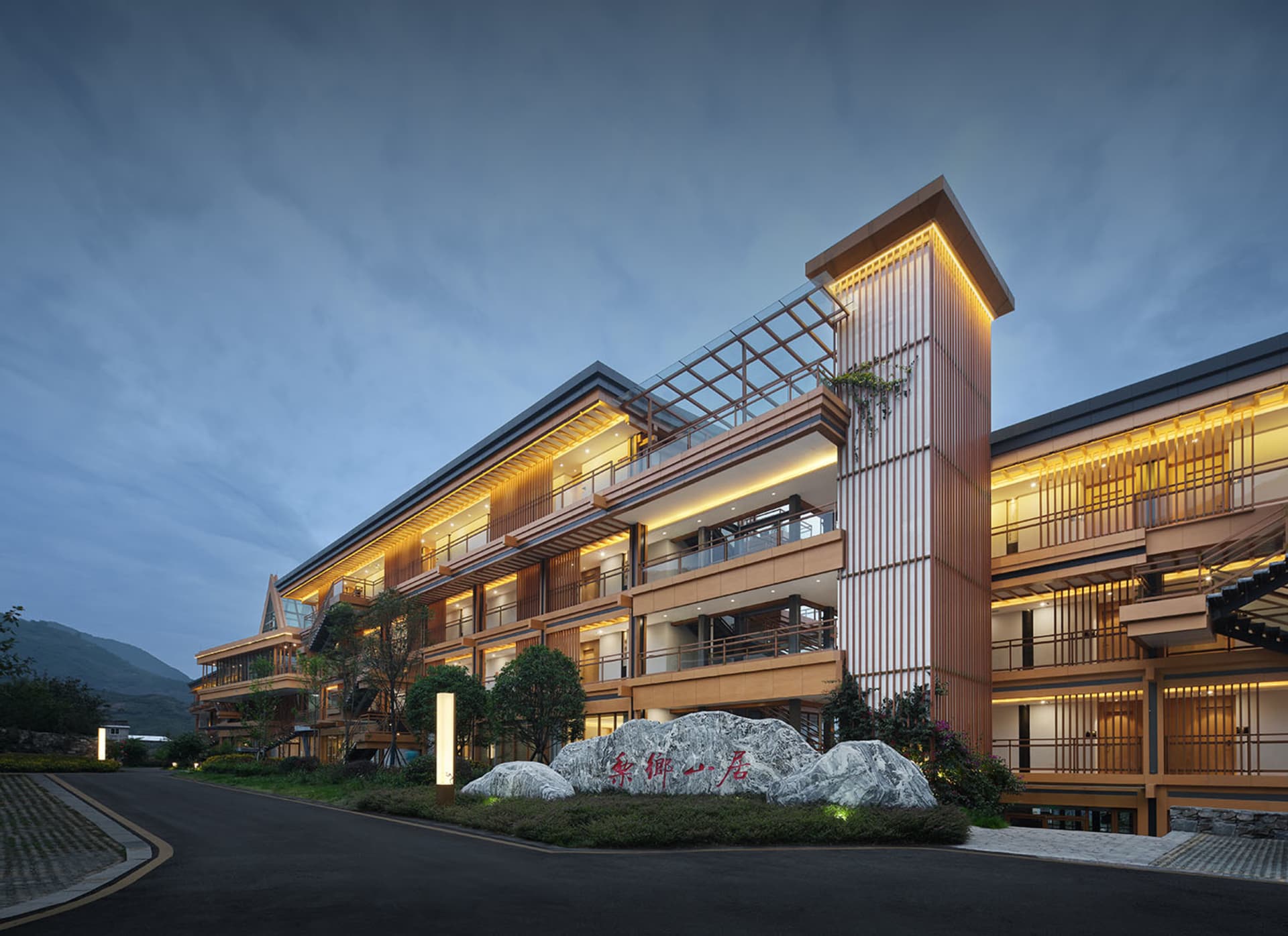 A modern hotel exterior with wooden structures, glass panels, and stone accents.