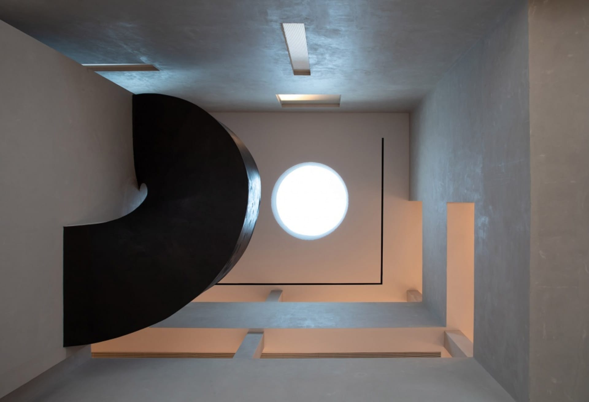 A minimalist, industrial-style spiral staircase made of black metal and concrete interiors with a circular window.