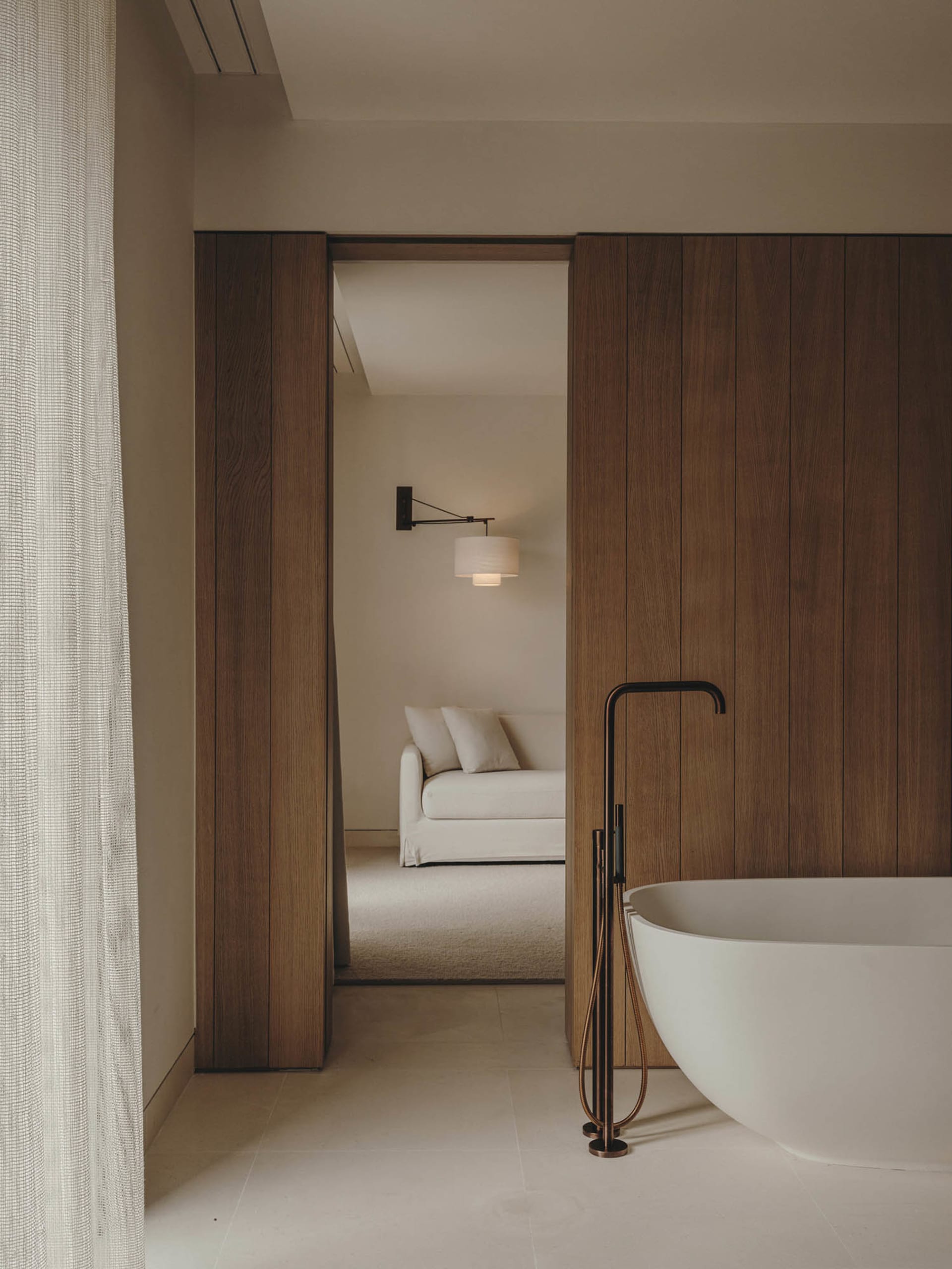Modern minimalist bathroom with white freestanding bathtub, wooden paneling, and white floor tiles.