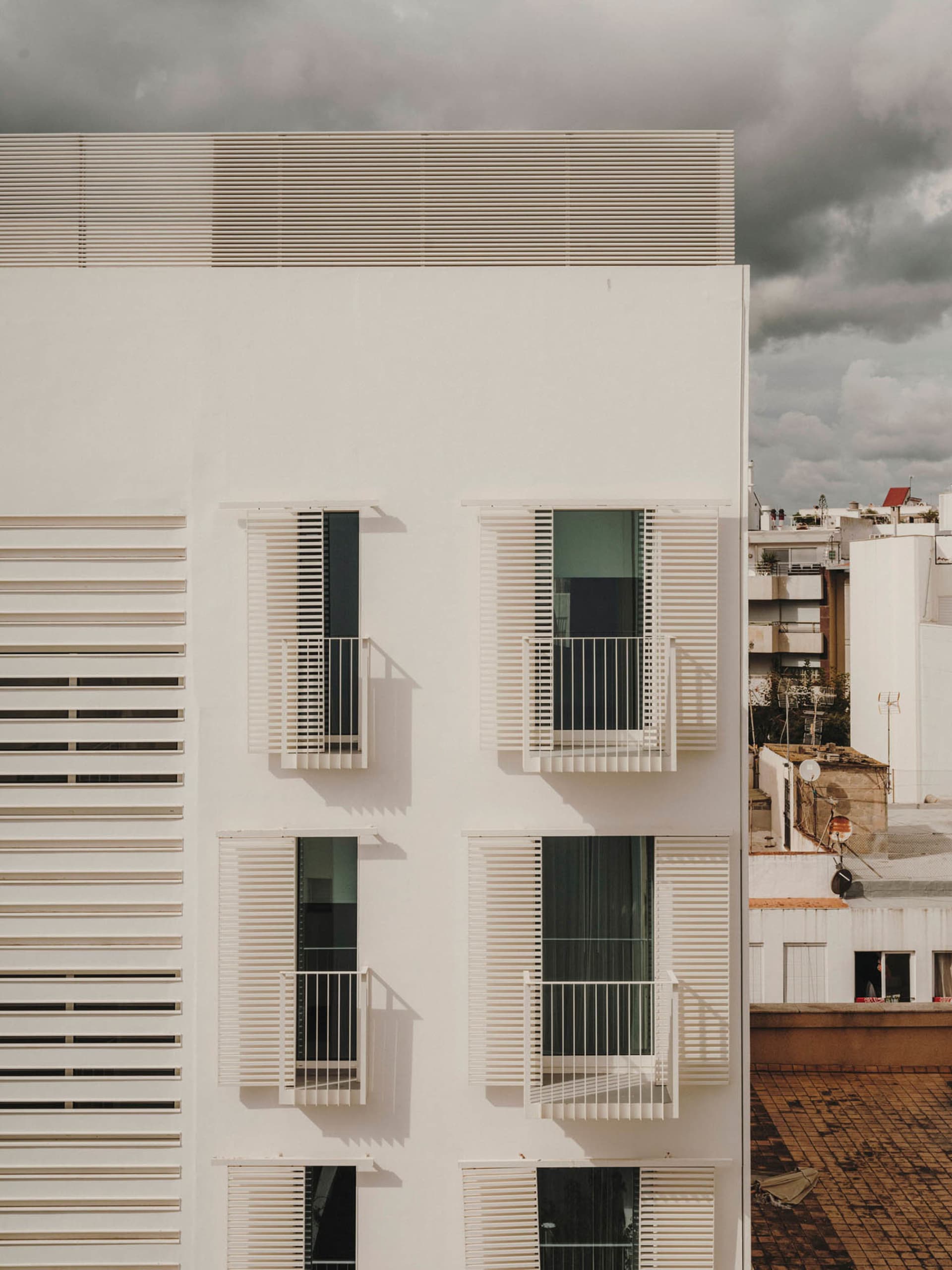 Modern residential building with white concrete exterior and white metal railings on balconies against a cloudy sky.