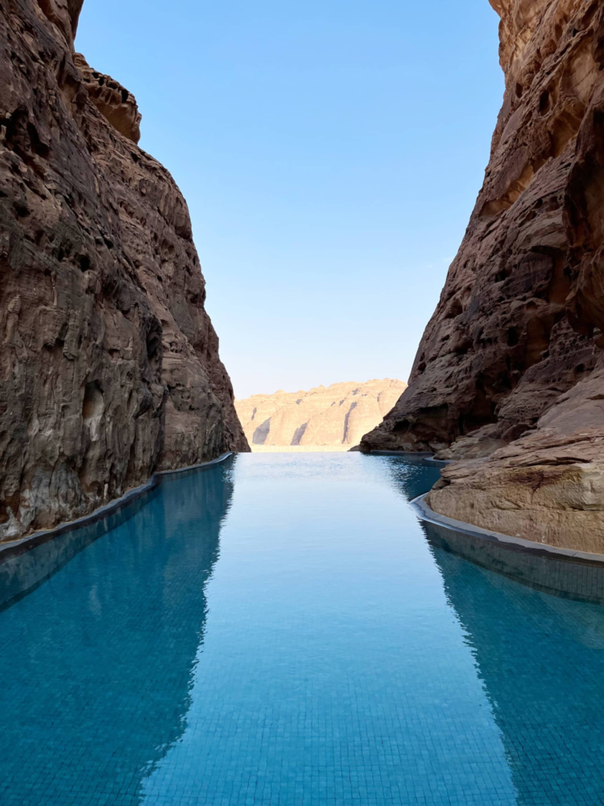 A serene swimming pool bordered by majestic rock formations under a clear blue sky.
