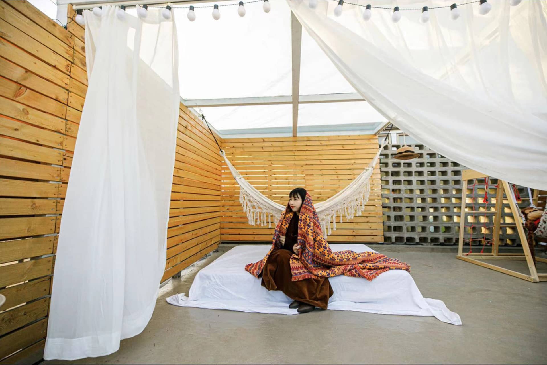 A woman sits on a relaxing space with textiles and a hammock
