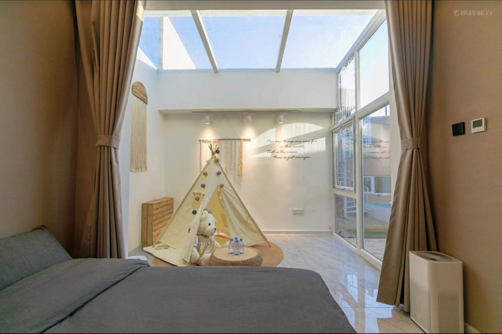 A modern bedroom featuring a comfortable bed, a playful children's tent on the floor, and a spacious window area with a view