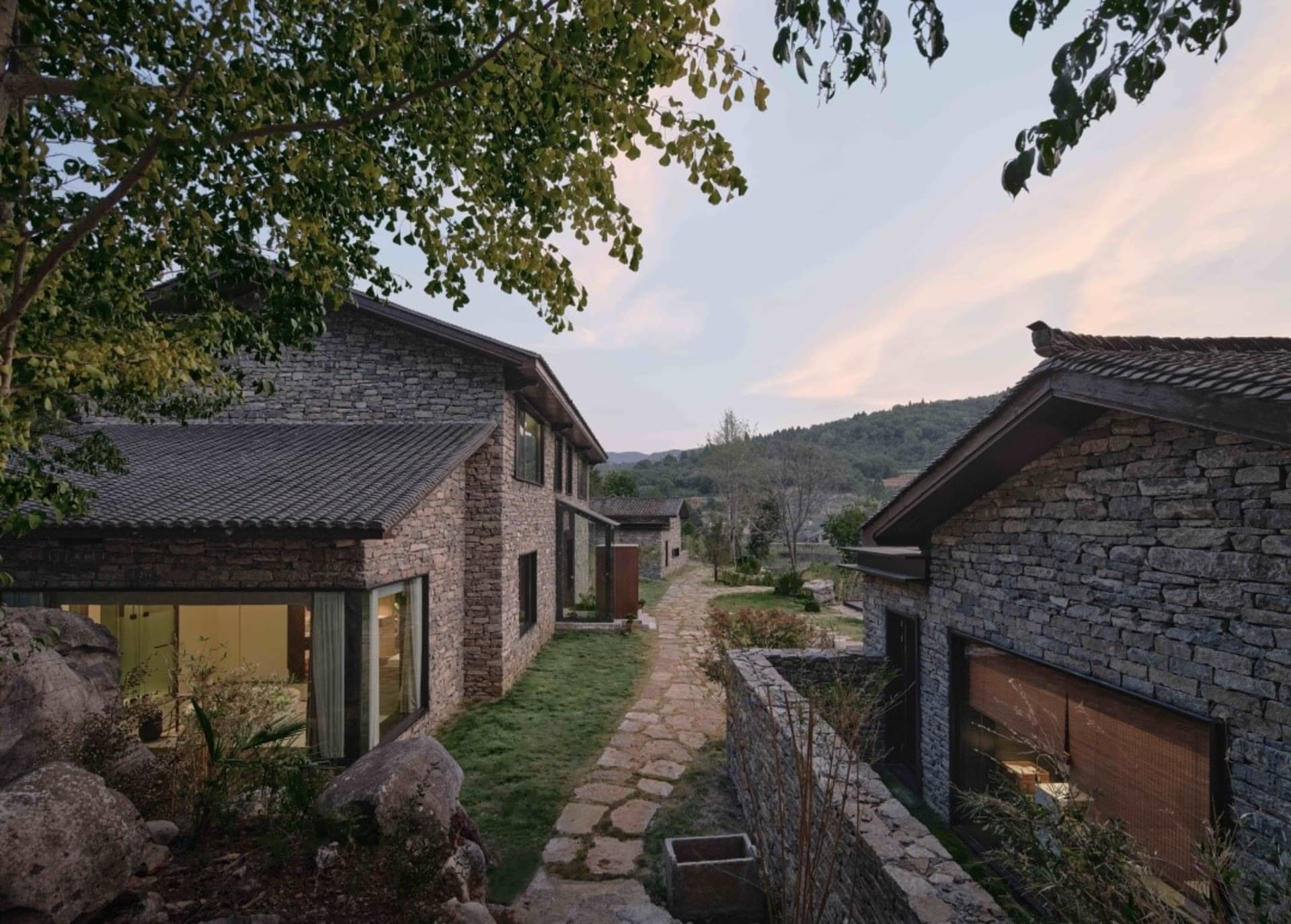 一棟現代住宅別墅，外牆採用石材搭配玻璃窗，環繞自然景觀。