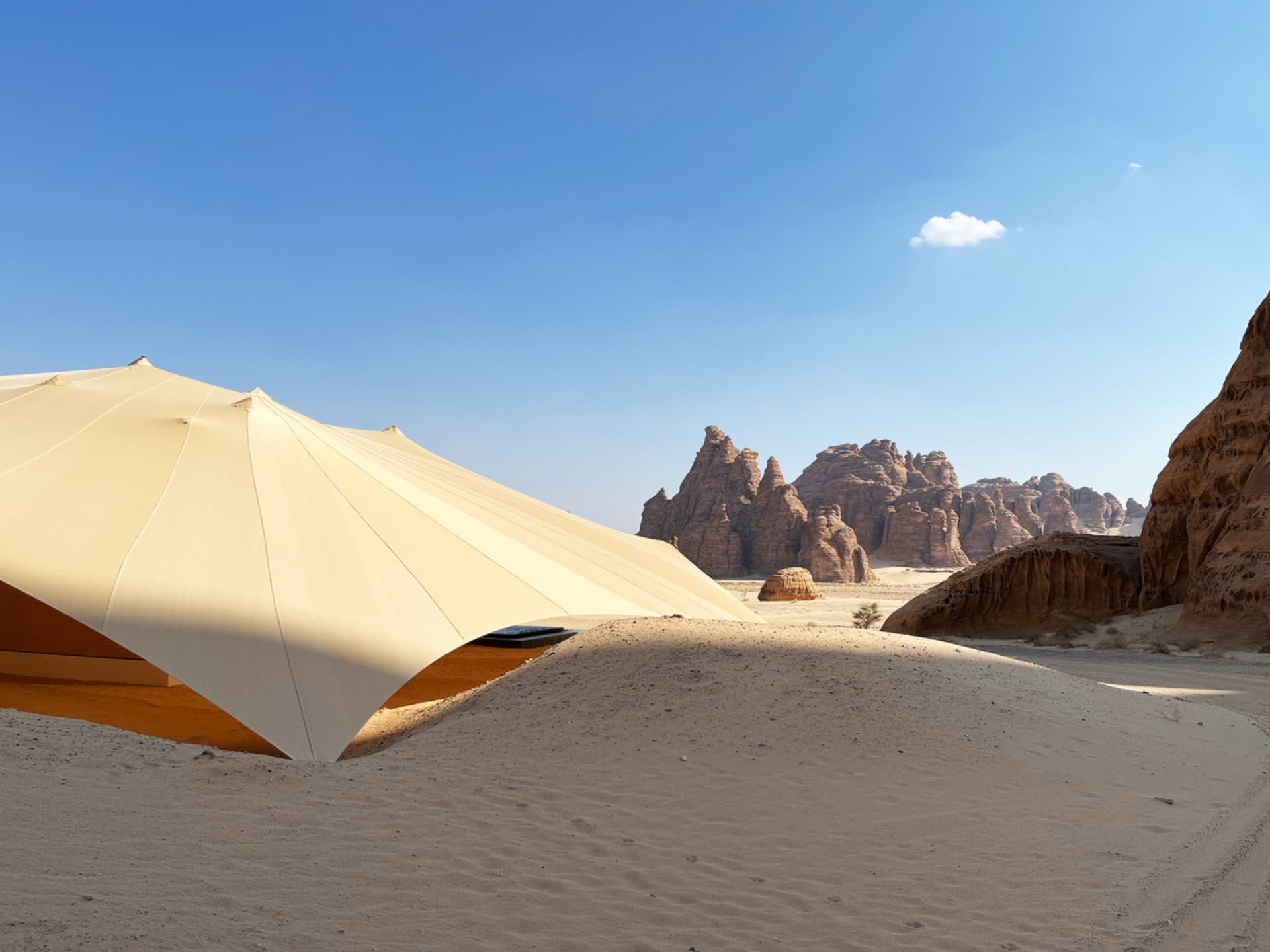 A modern tent structure in a desert landscape with a sandstone background.
