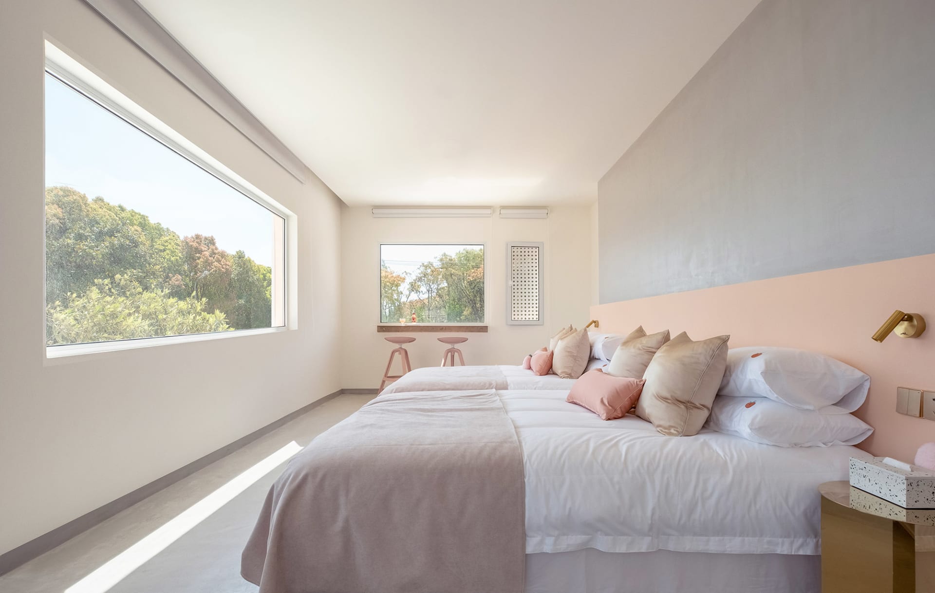 A minimalist bedroom with concrete walls, a large window, and soft pink accents on the bed and headboard.