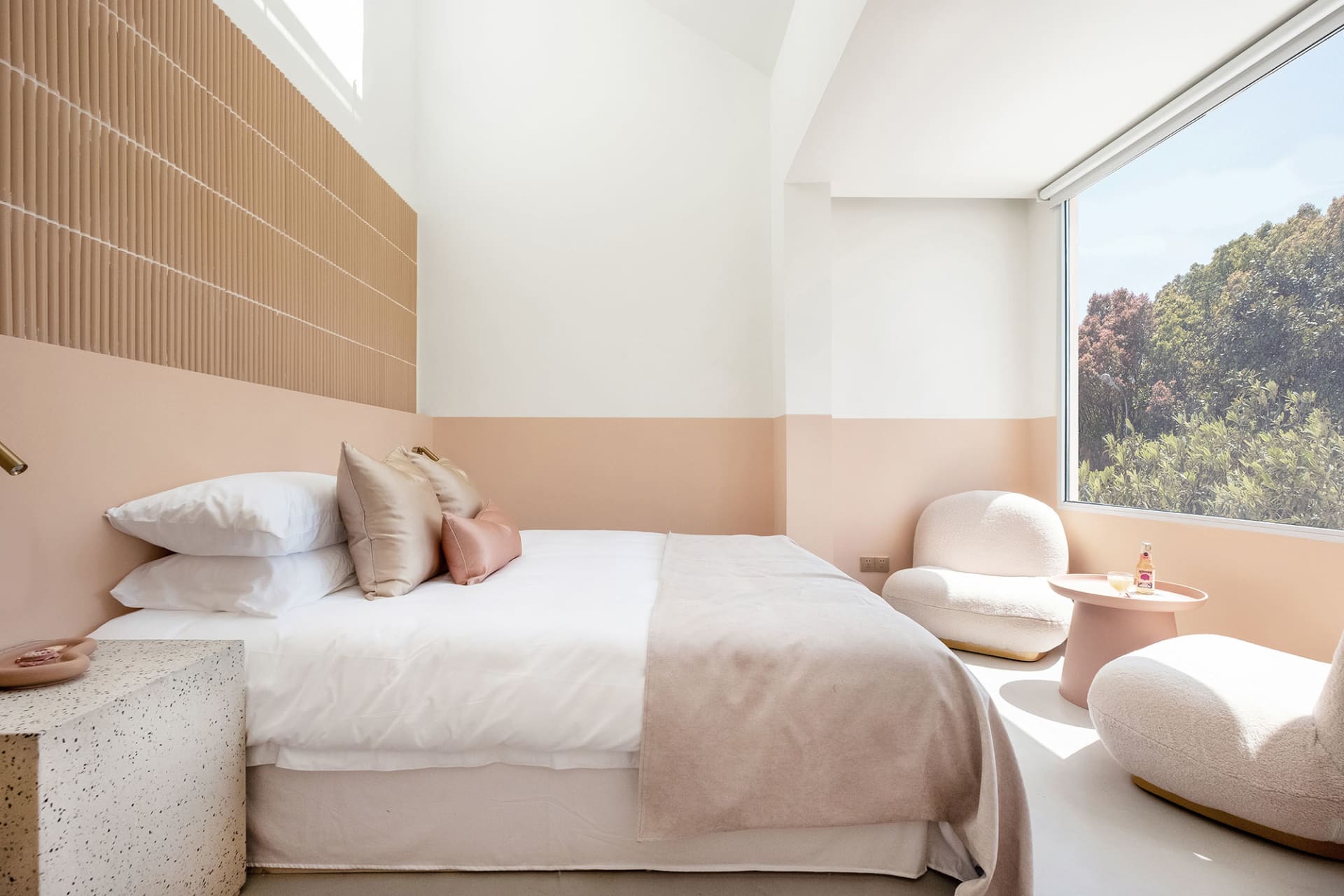 A modern bedroom featuring a bed with white bedding, white-cement walls, and a view of trees through a window.