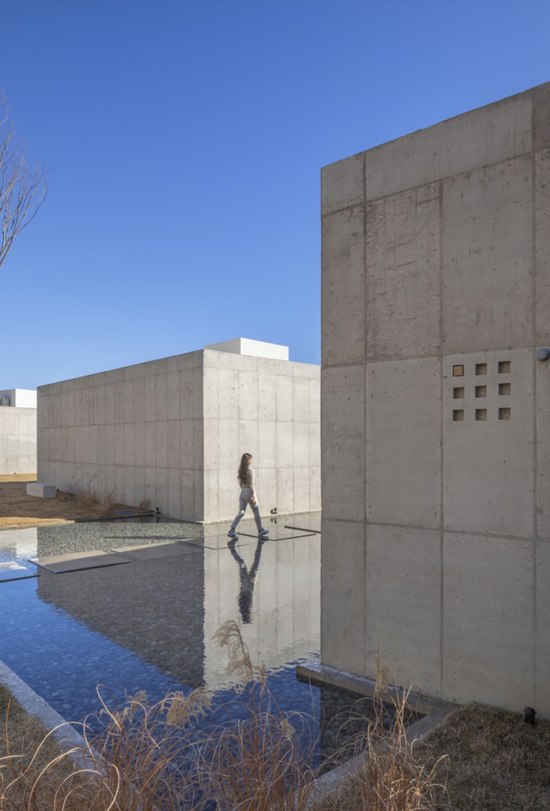 A modern building with a concrete exterior features clean lines and a minimalist design, surrounded by a large reflecting poo