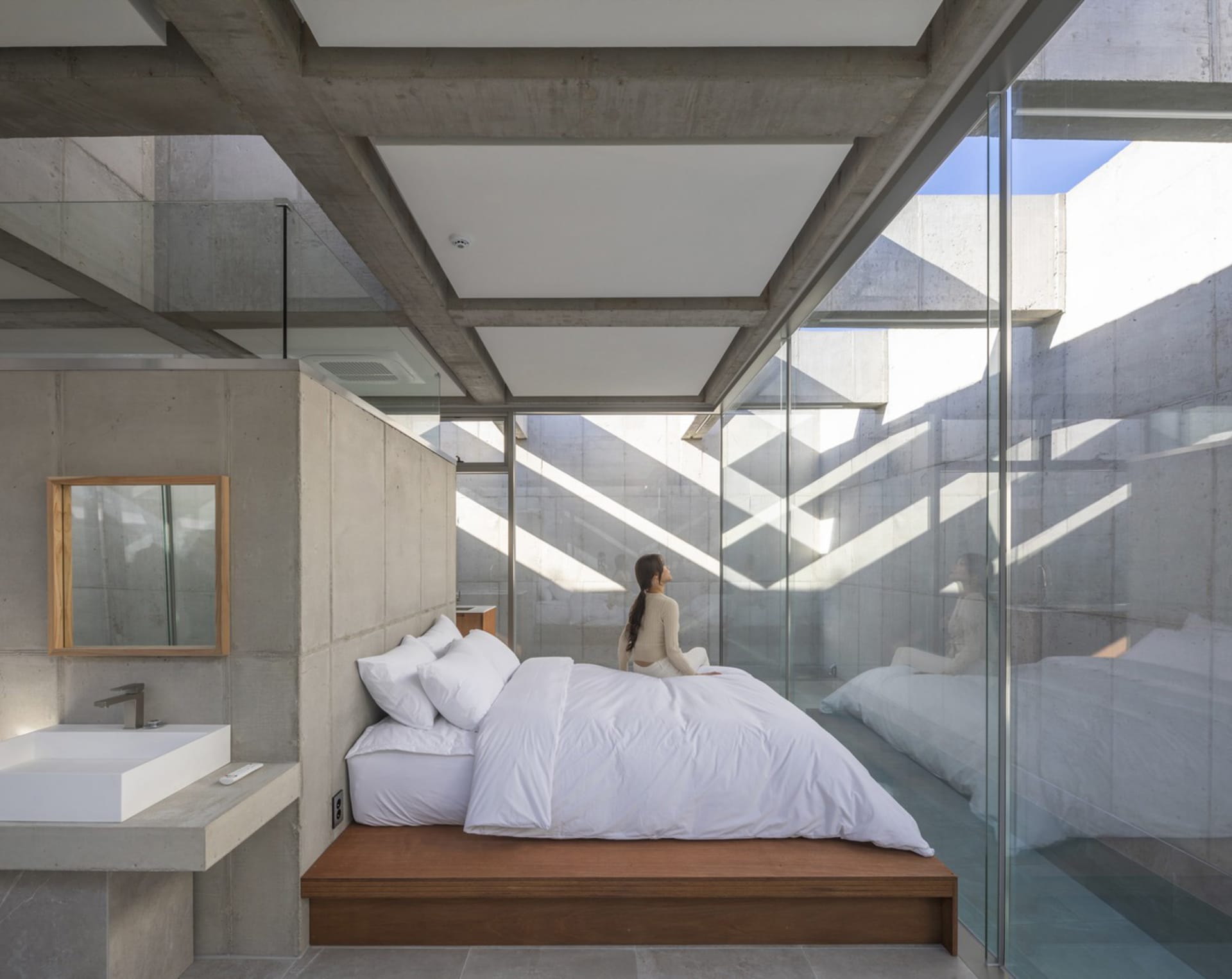 A minimalist bedroom with concrete walls, a wooden platform bed, and a white duvet.