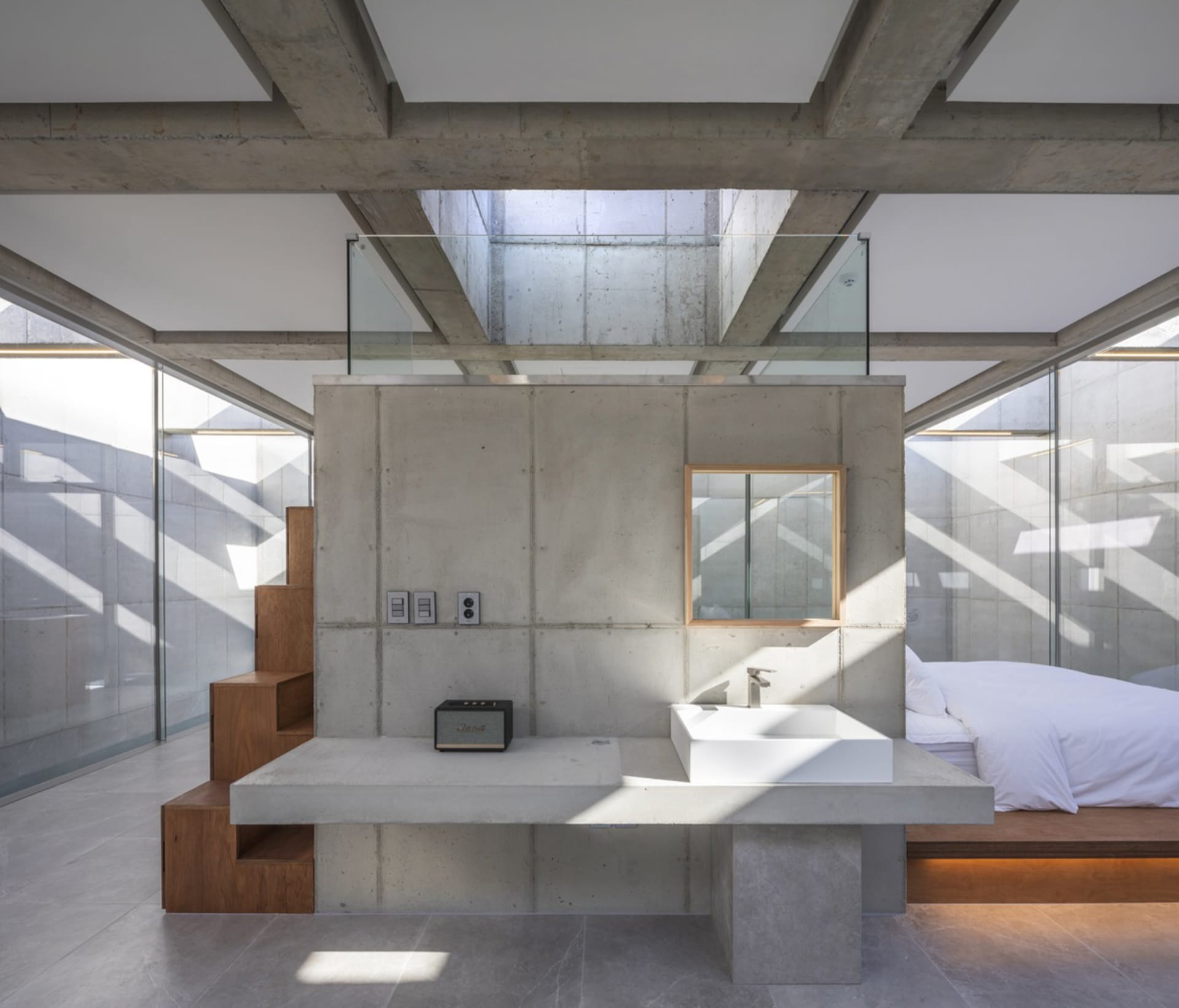 Modern minimalist bedroom featuring a bed with a white mattress and pillows, a sink on a concrete vanity, and a concrete wall