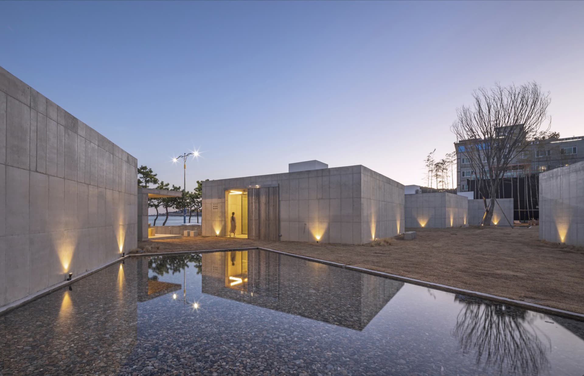 現代極簡建築外觀,混凝土牆面搭配倒影水池,黃昏時分由聚光燈照亮