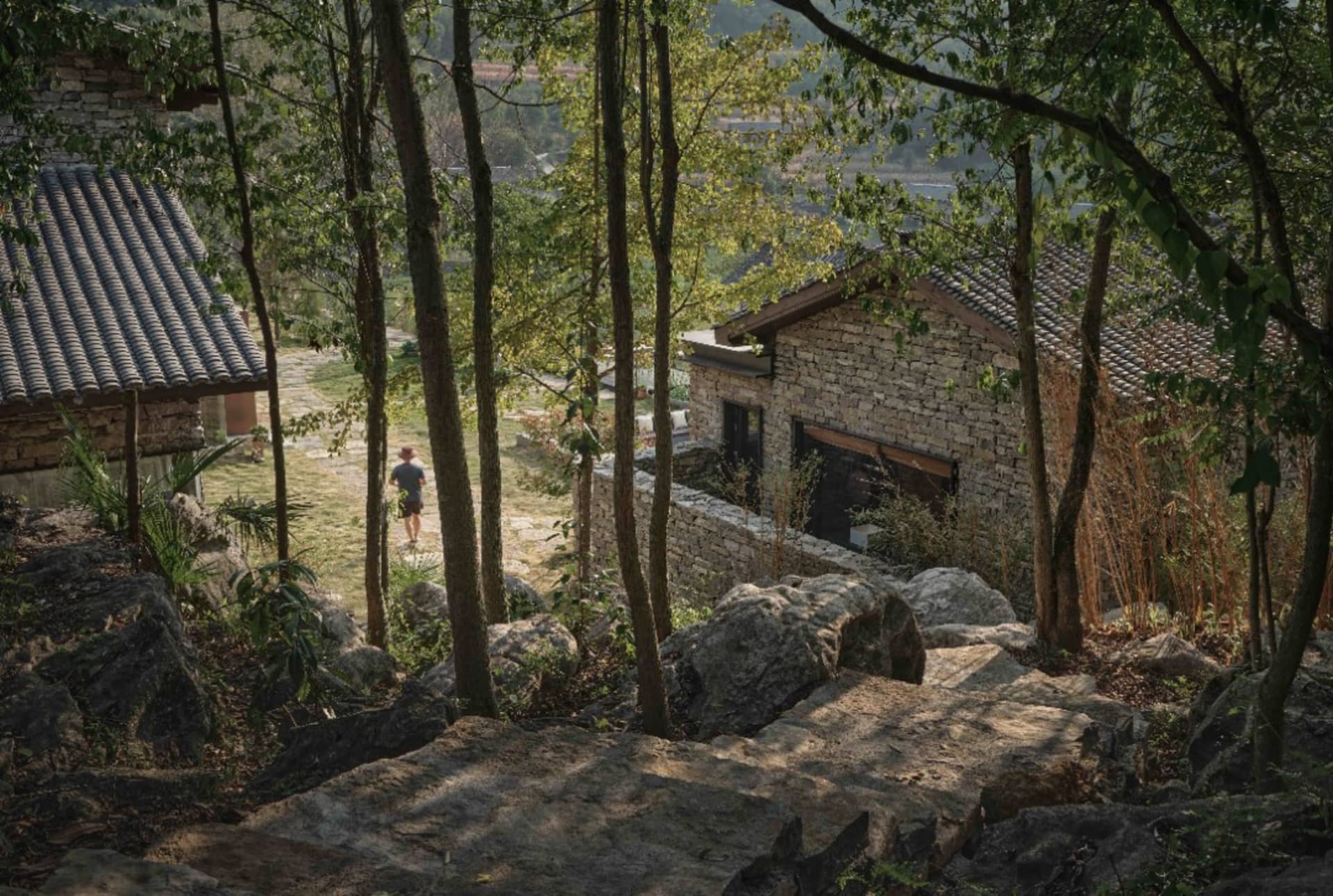 一座覆以石材的建築坐落於自然景觀中，伴隨著樹木與岩石。