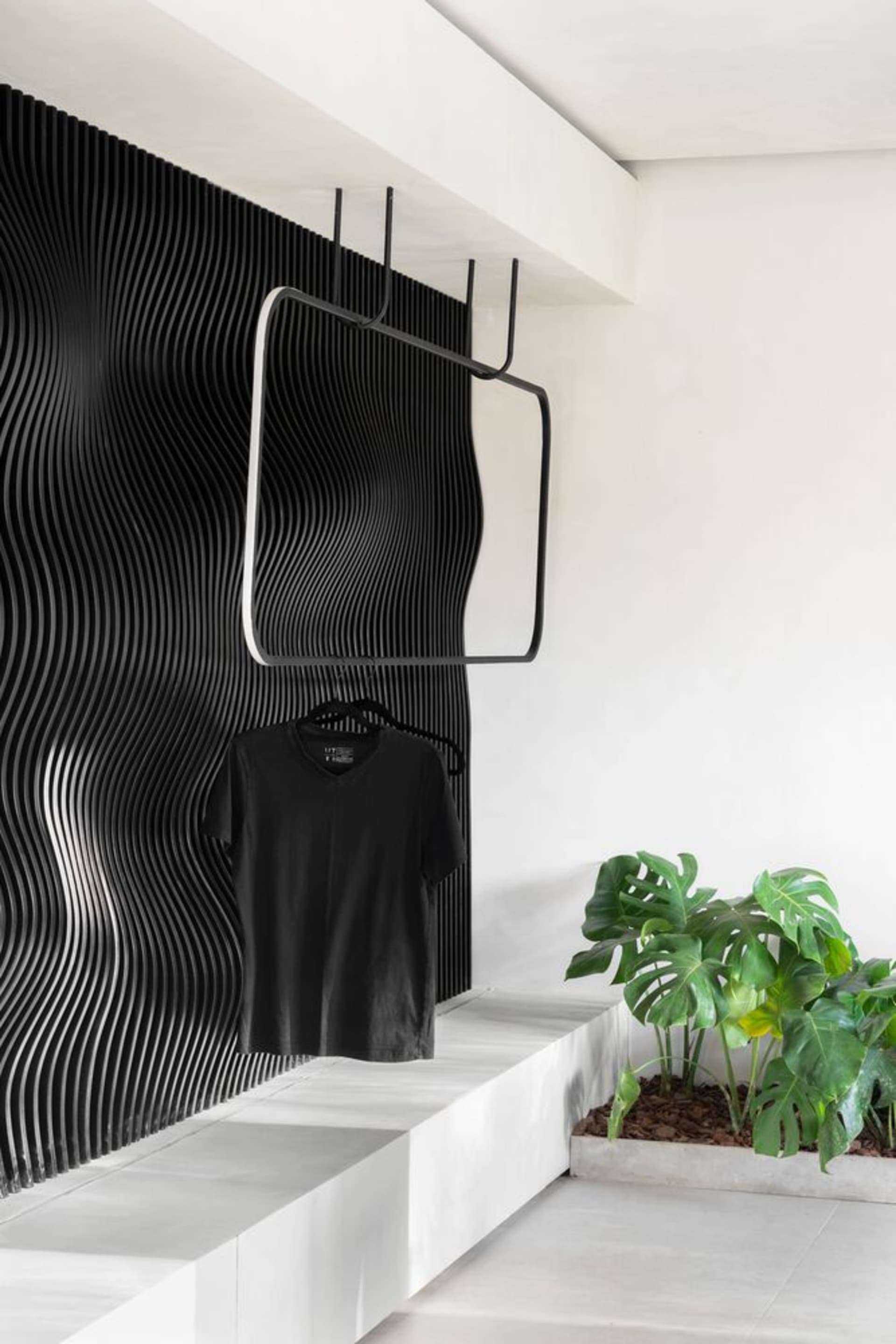 Black metal clothing rack with wave-pattern on textured white wall and green plant in planter