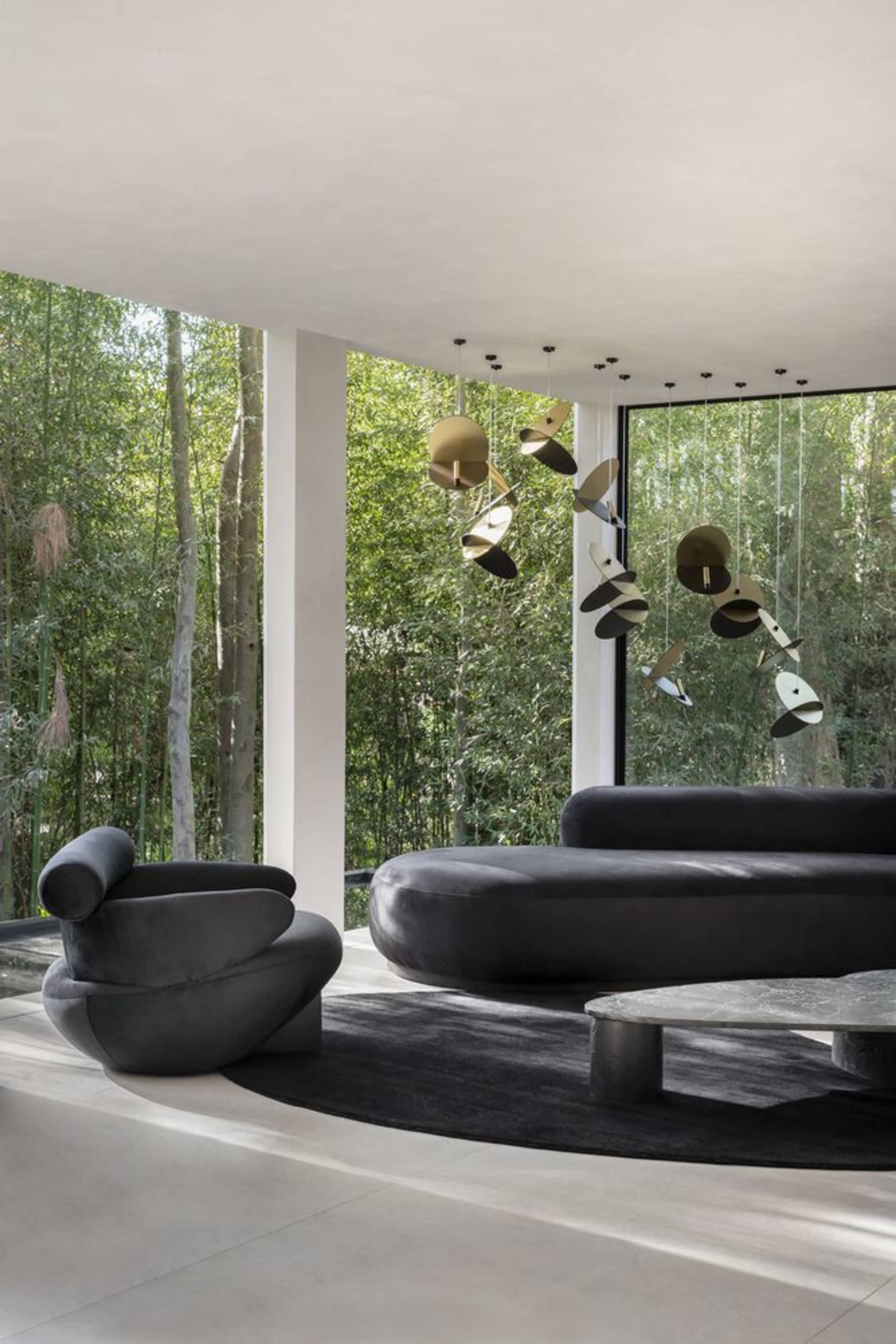 Modern living room featuring sleek, black furniture, large windows, and a hanging art installation