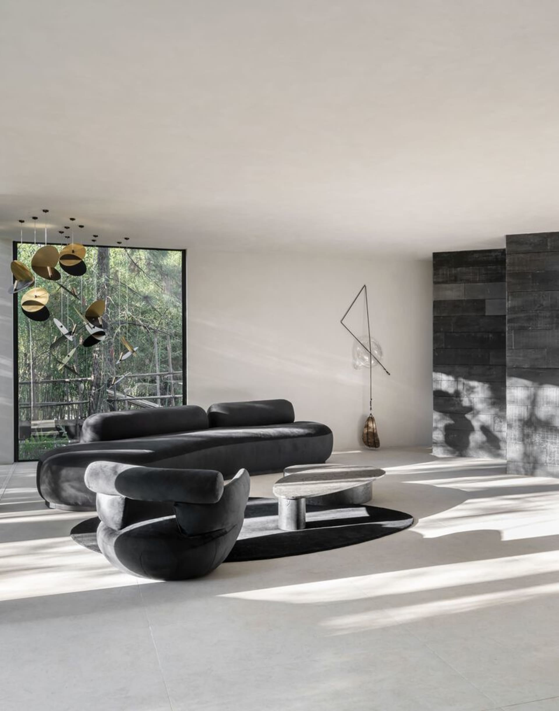 A sleek, modern living room with concrete flooring, glass walls, and metal elements, featuring a dark, curved sofa and a scul
