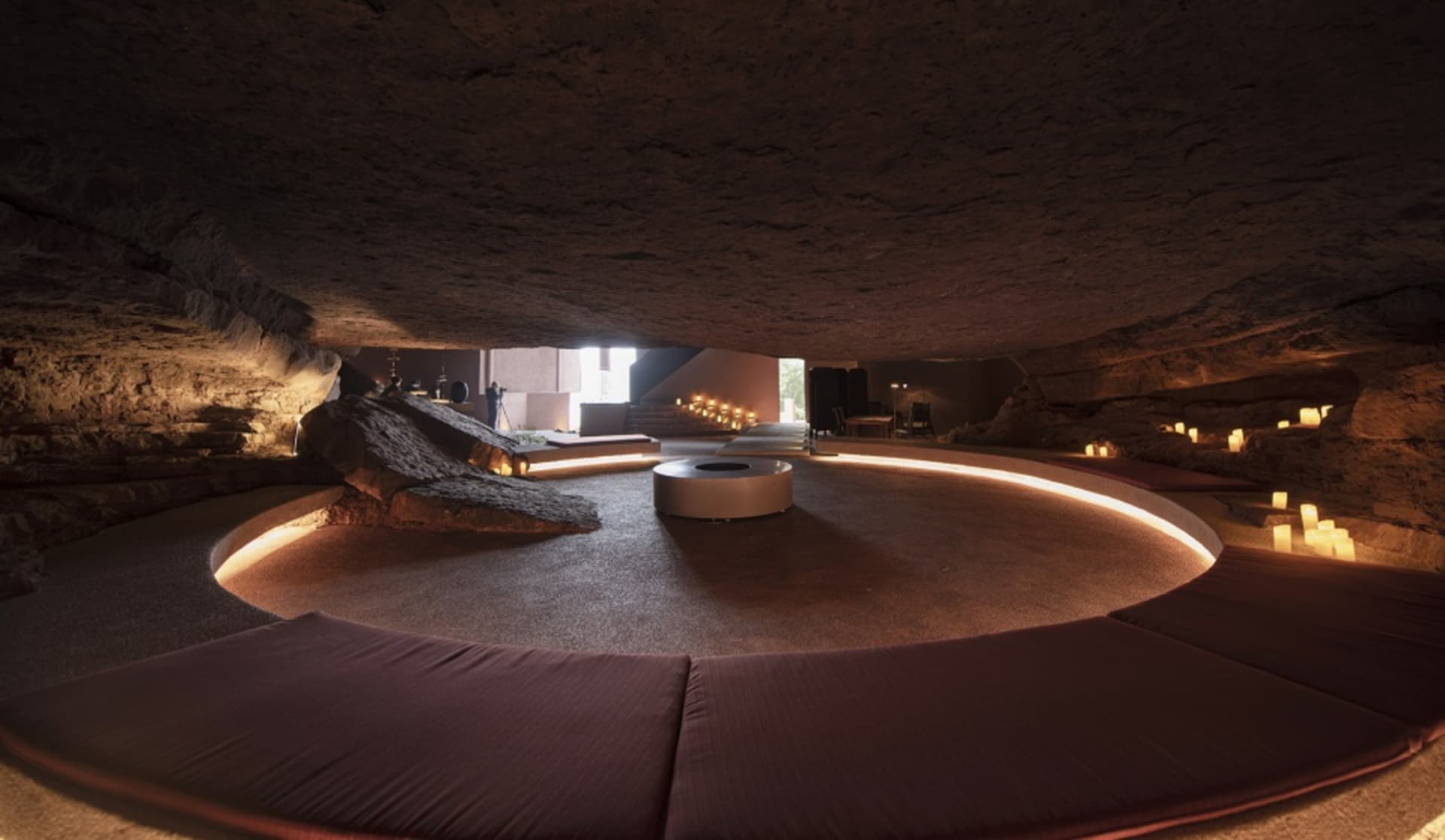 Circular space with industrial design elements, including exposed ceiling and rock formations, illuminated by warm lighting a