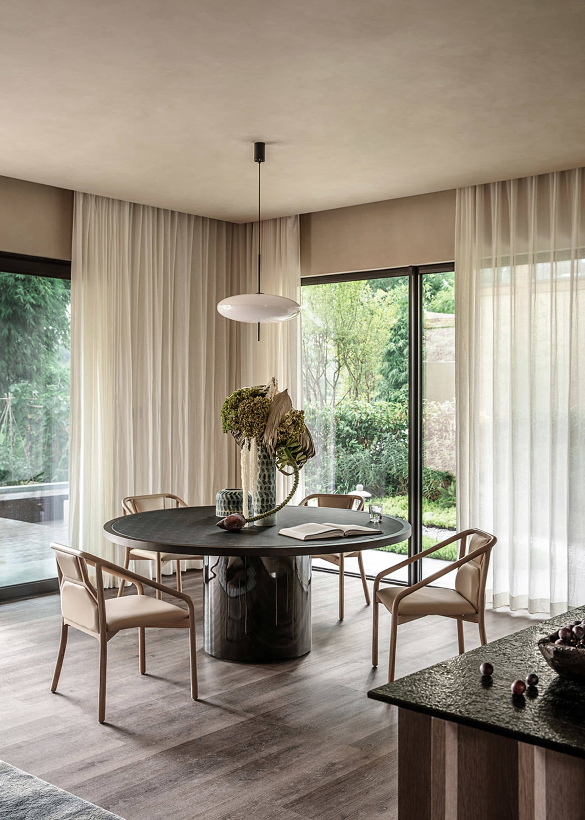 A modern minimalist dining room with a round table, wood chairs, and a hanging pendant light.