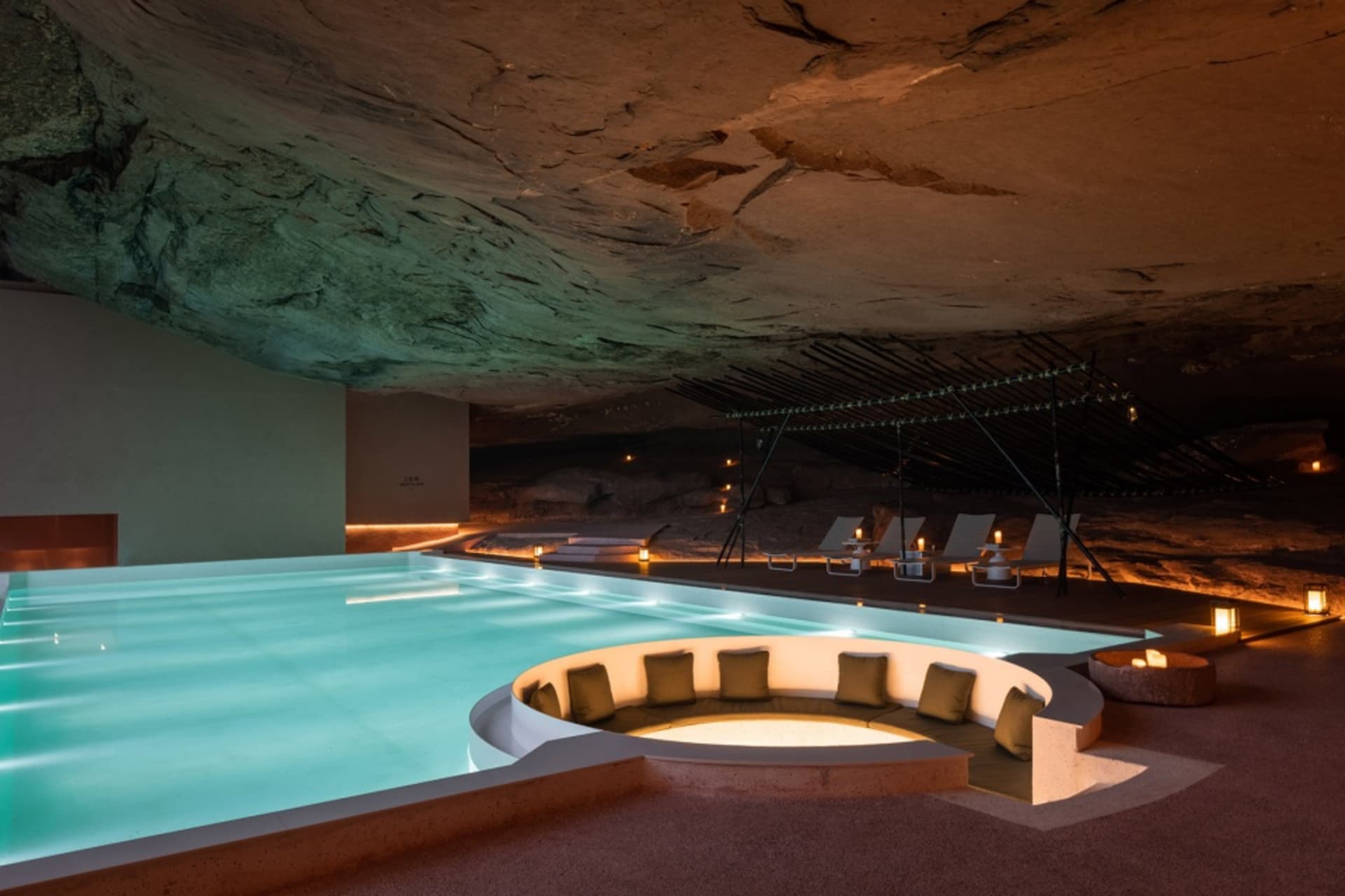 A modern minimalist swimming pool integrated into a rock formation, featuring concrete materials and a circular seating area.