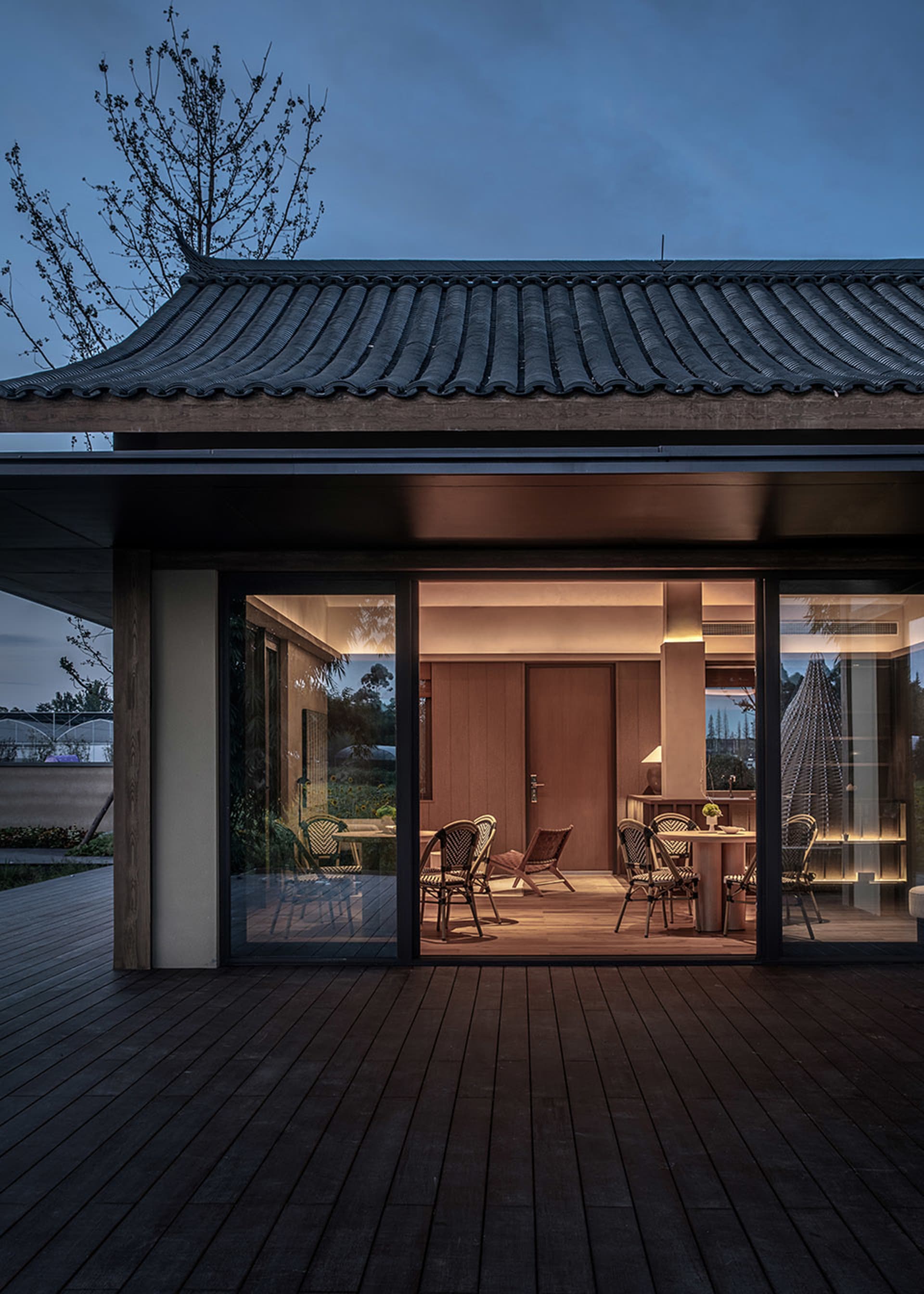 A traditional-style outdoor dining area with dark wooden flooring and a wooden roof, illuminated at dusk.