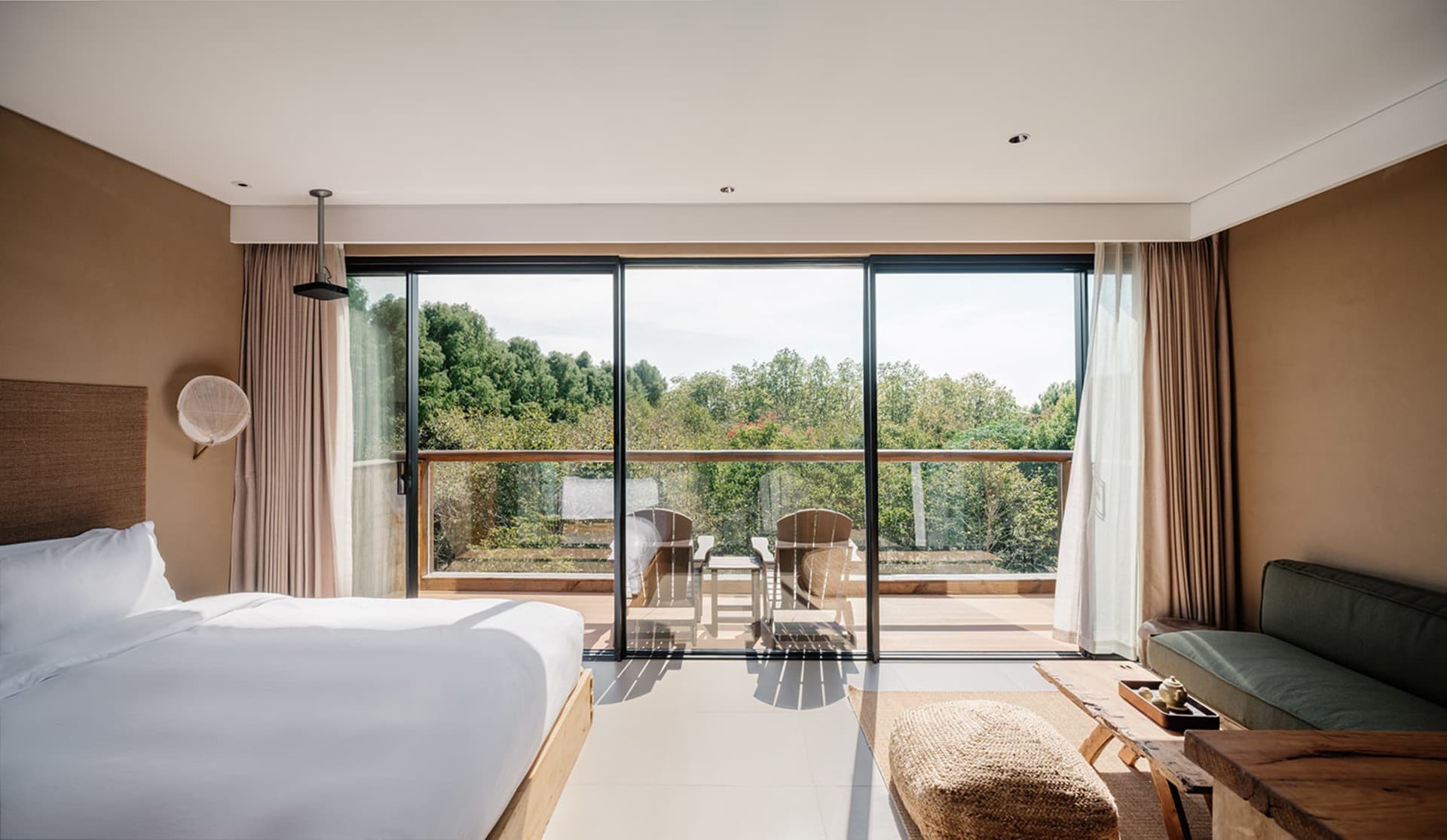 A modern minimalist bedroom featuring a large window with glass doors leading to a balcony overlooking trees.