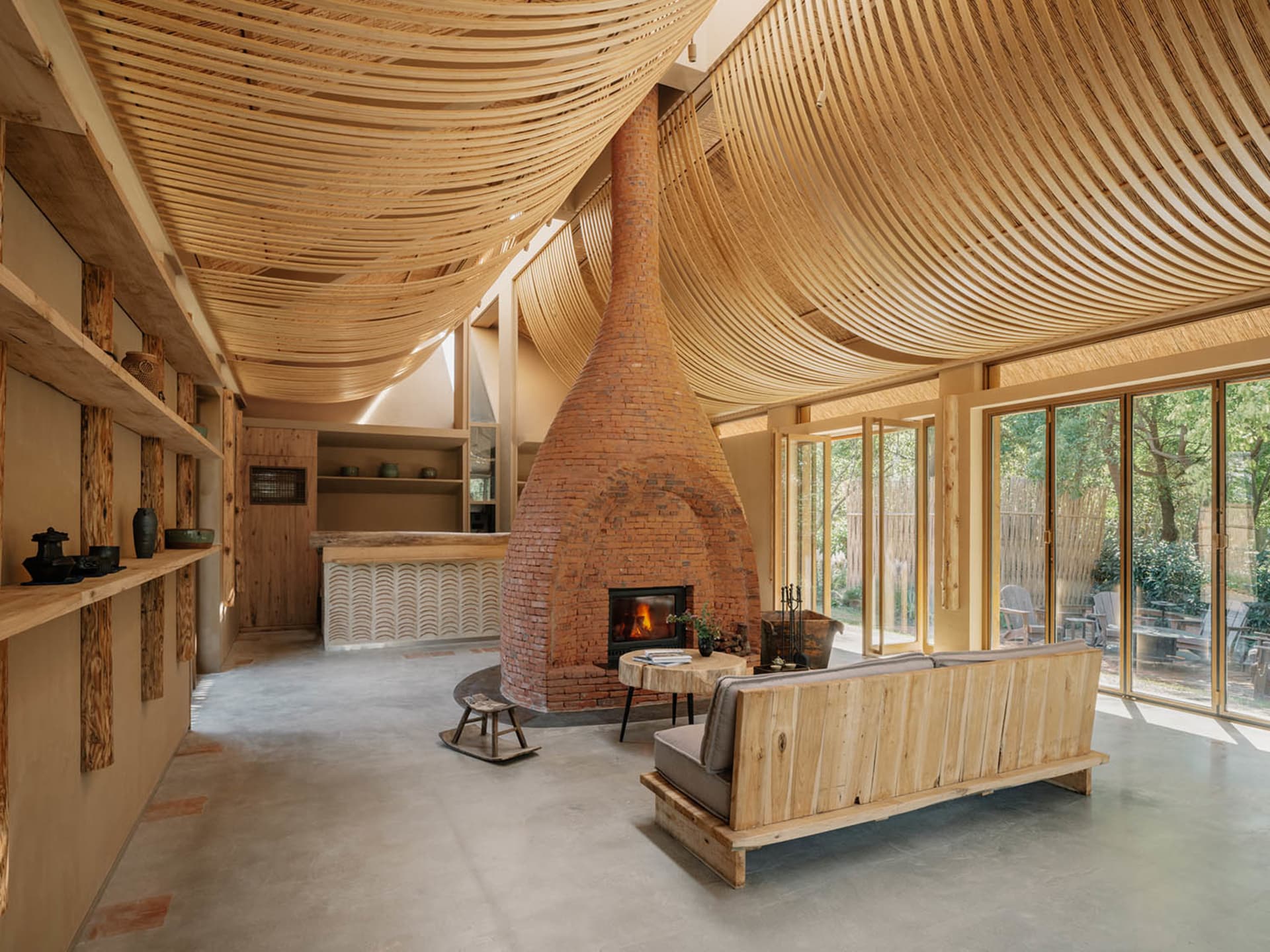 A modern industrial living room with wooden elements, a brick fireplace, and large windows.