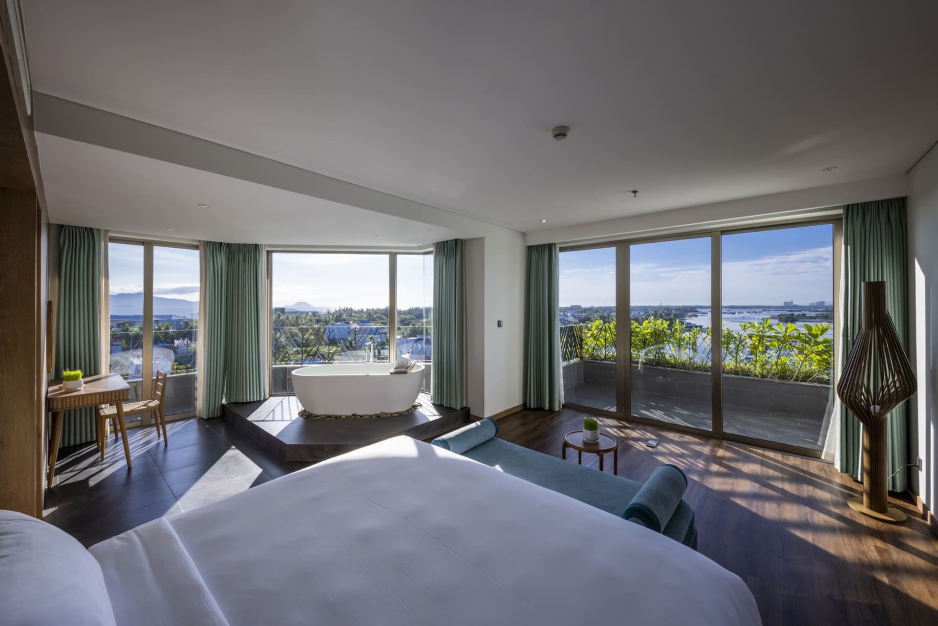 Modern bedroom with black flooring, leather seating, and floor-to-ceiling windows overlooking a scenic view.
