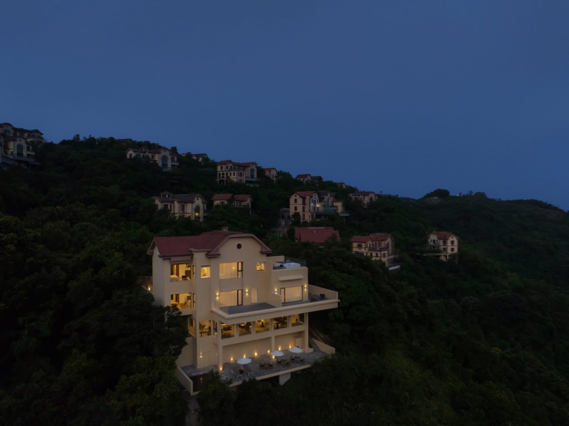 夜晚燈光照亮的現代住宅,擁有磚牆外觀與舒適的戶外座椅。