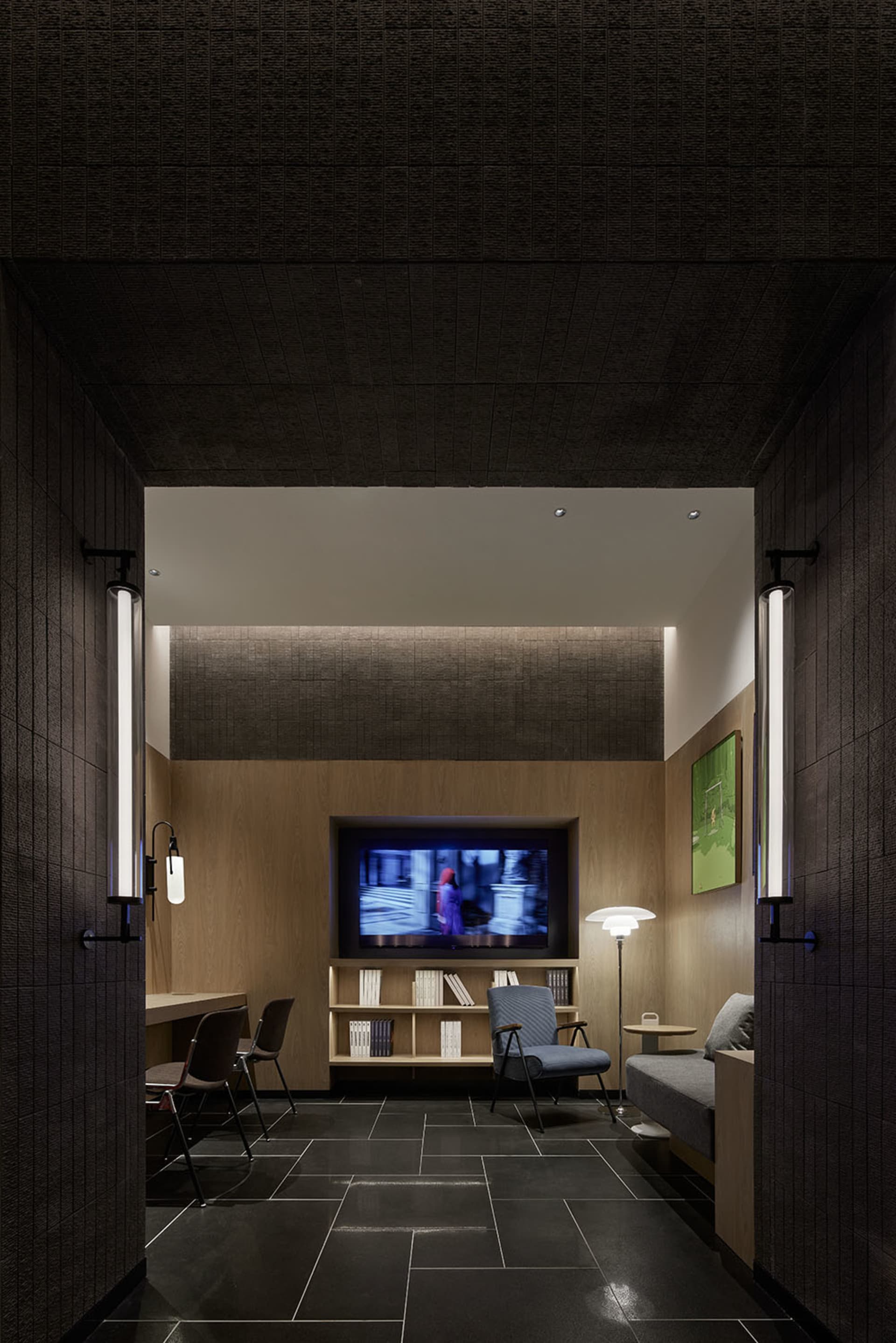 A modern interior design featuring a dark-themed TV room with a wooden accent wall, bookshelves, and a comfortable seating ar