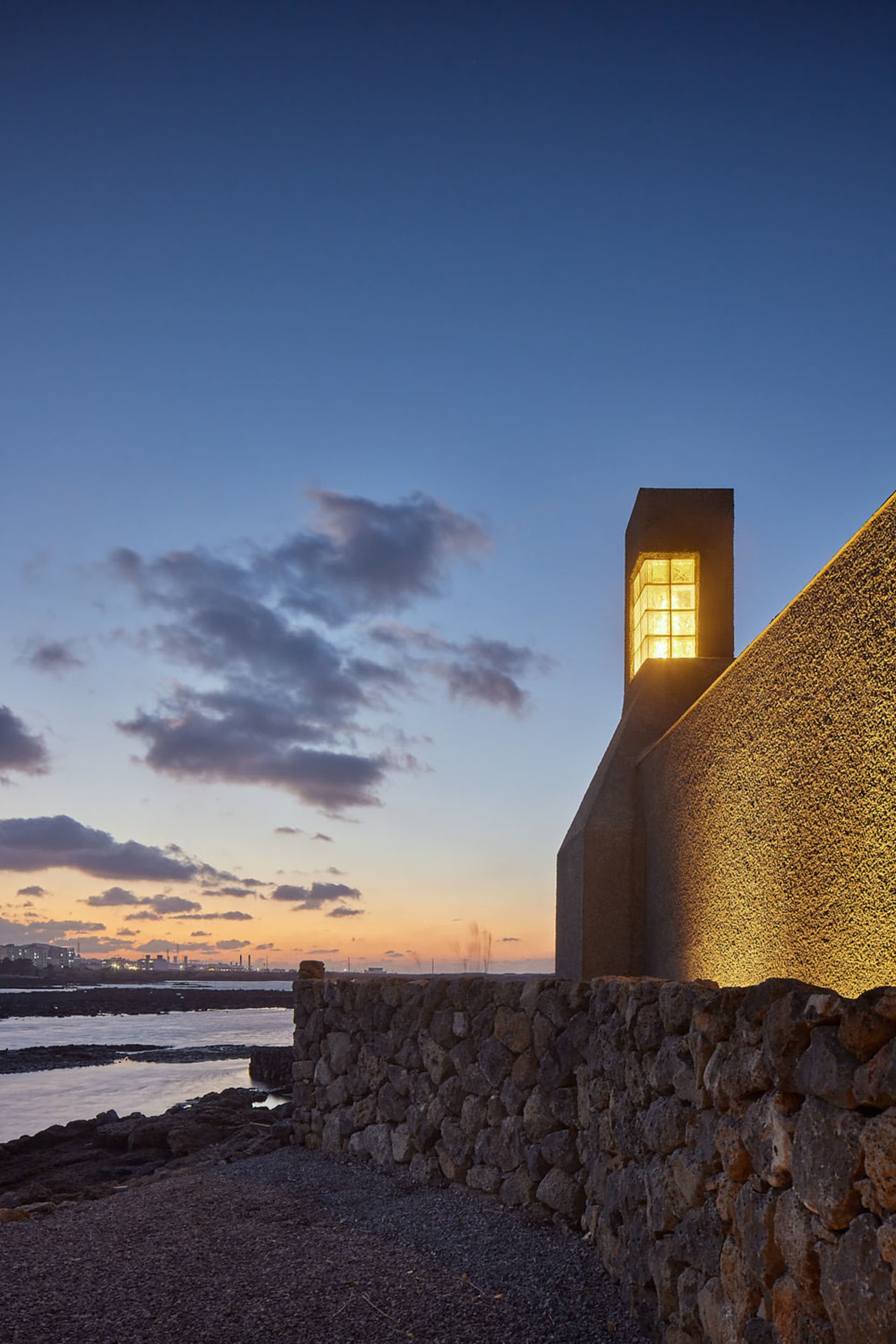 A modern building with concrete exterior illuminated by warm light against a twilight sky.