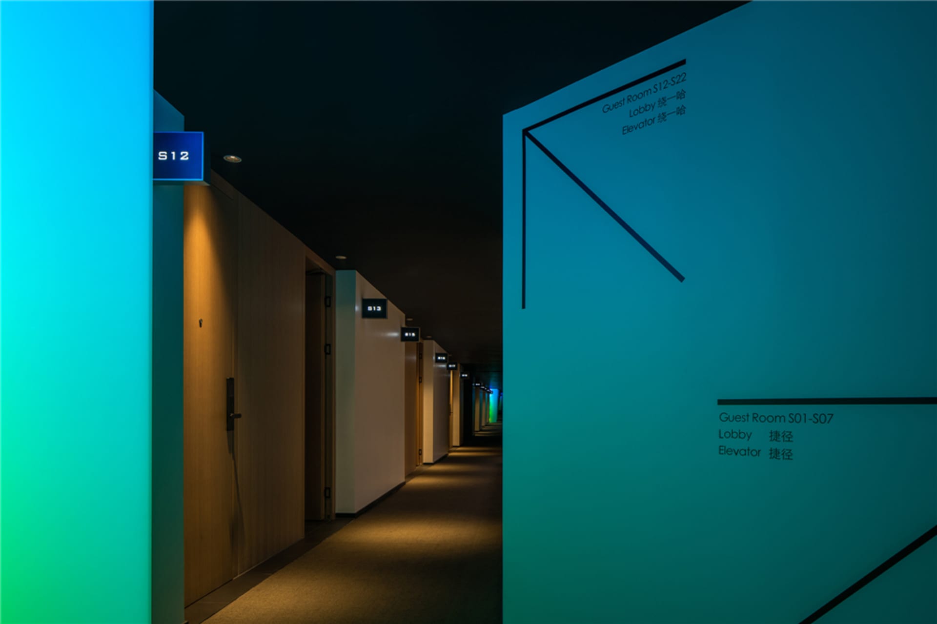 A modern hotel hallway illuminated with warm lighting, featuring room signs and directional arrows.