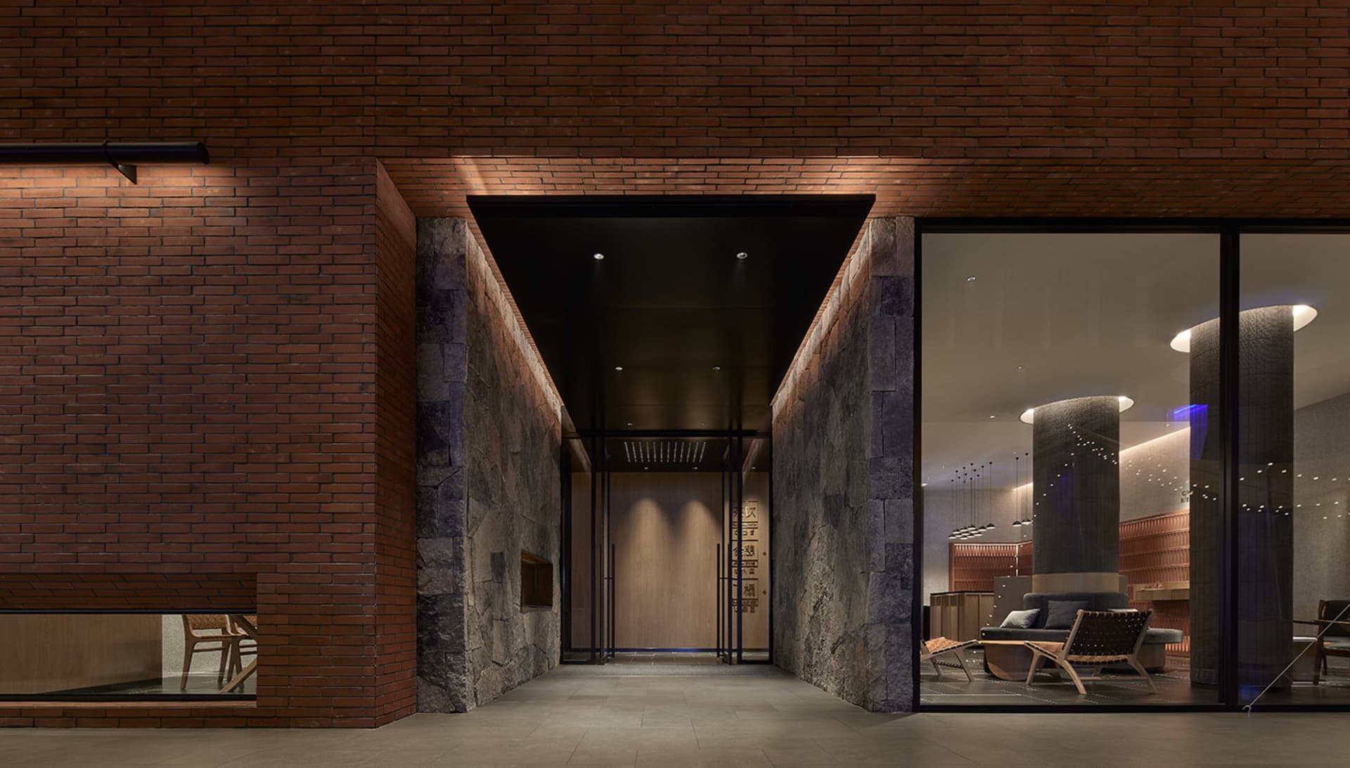Modern hotel lobby with brick walls and concrete pillars, illuminated by warm lighting.
