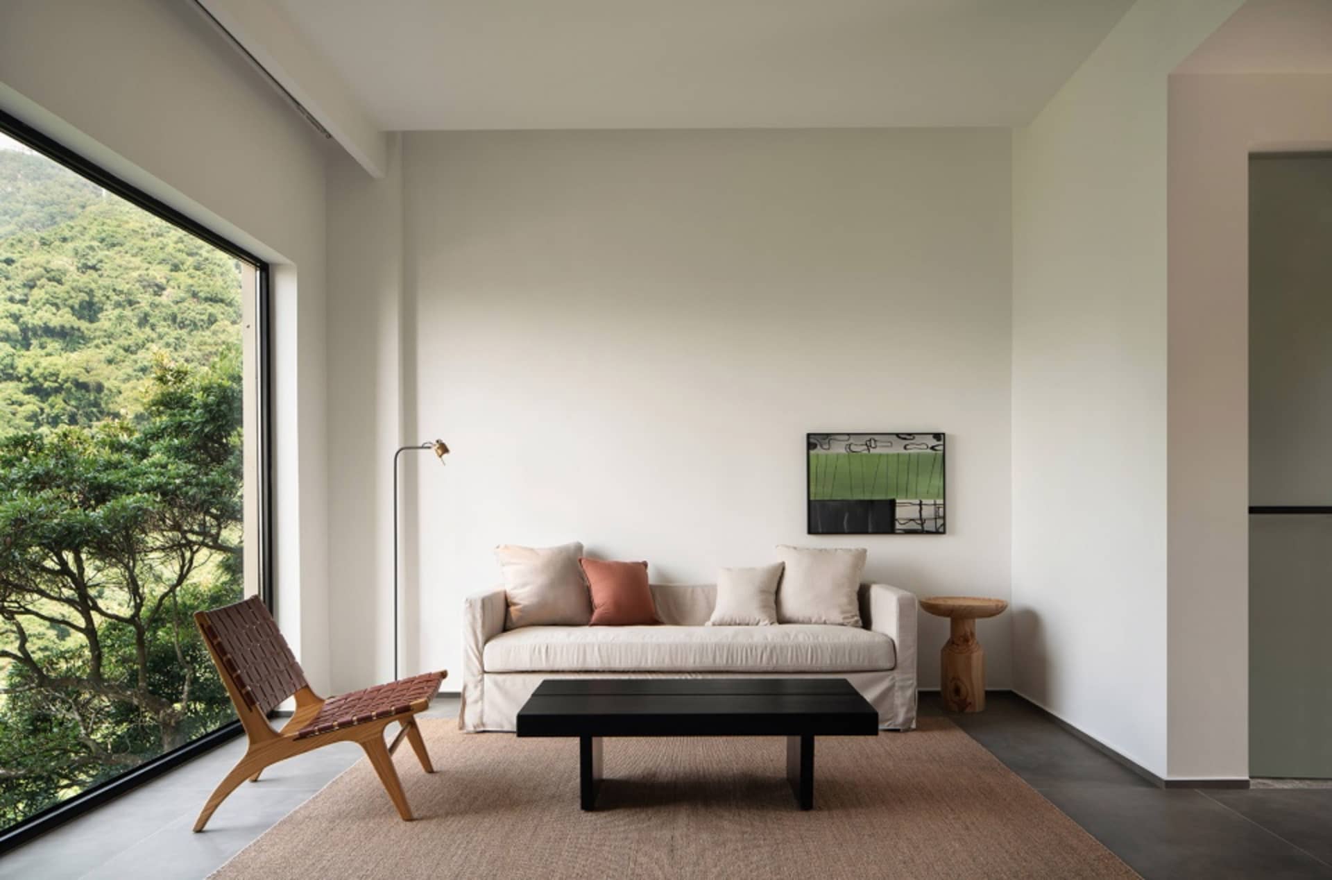 Modern minimalist living room with a white sofa, black coffee table, and a view of the mountains.