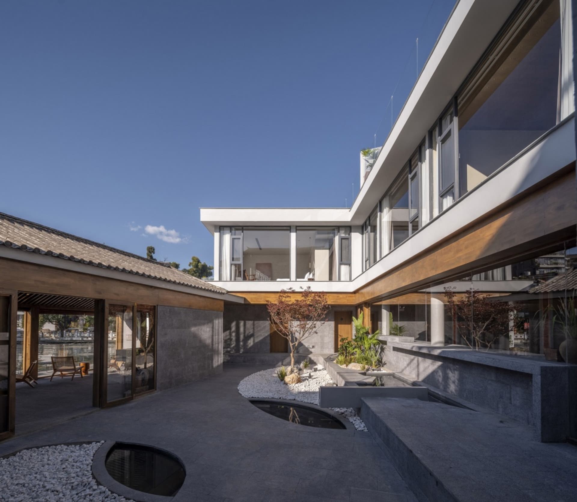 A modern residential exterior with concrete walls, glass windows, and a landscaped courtyard