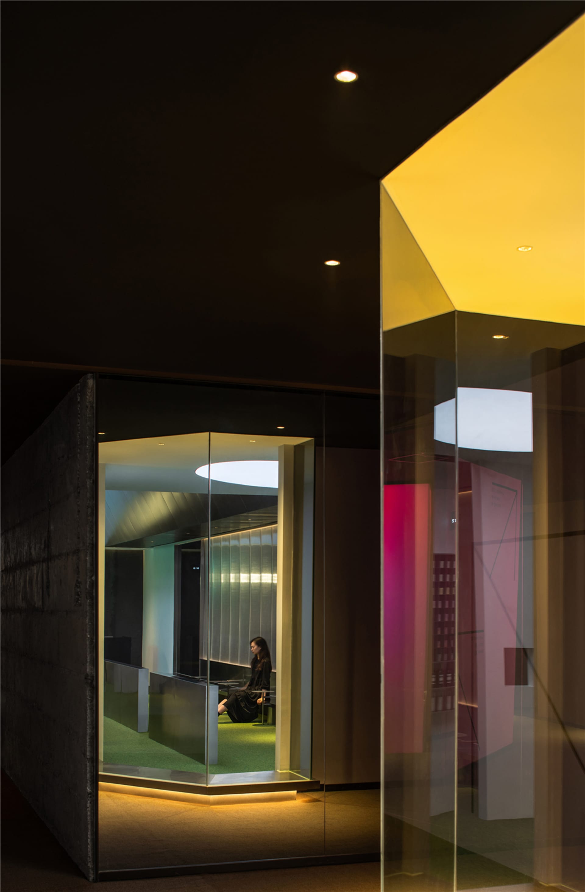 Modern minimalist office space with glass walls and concrete features, illuminated by LED lighting.