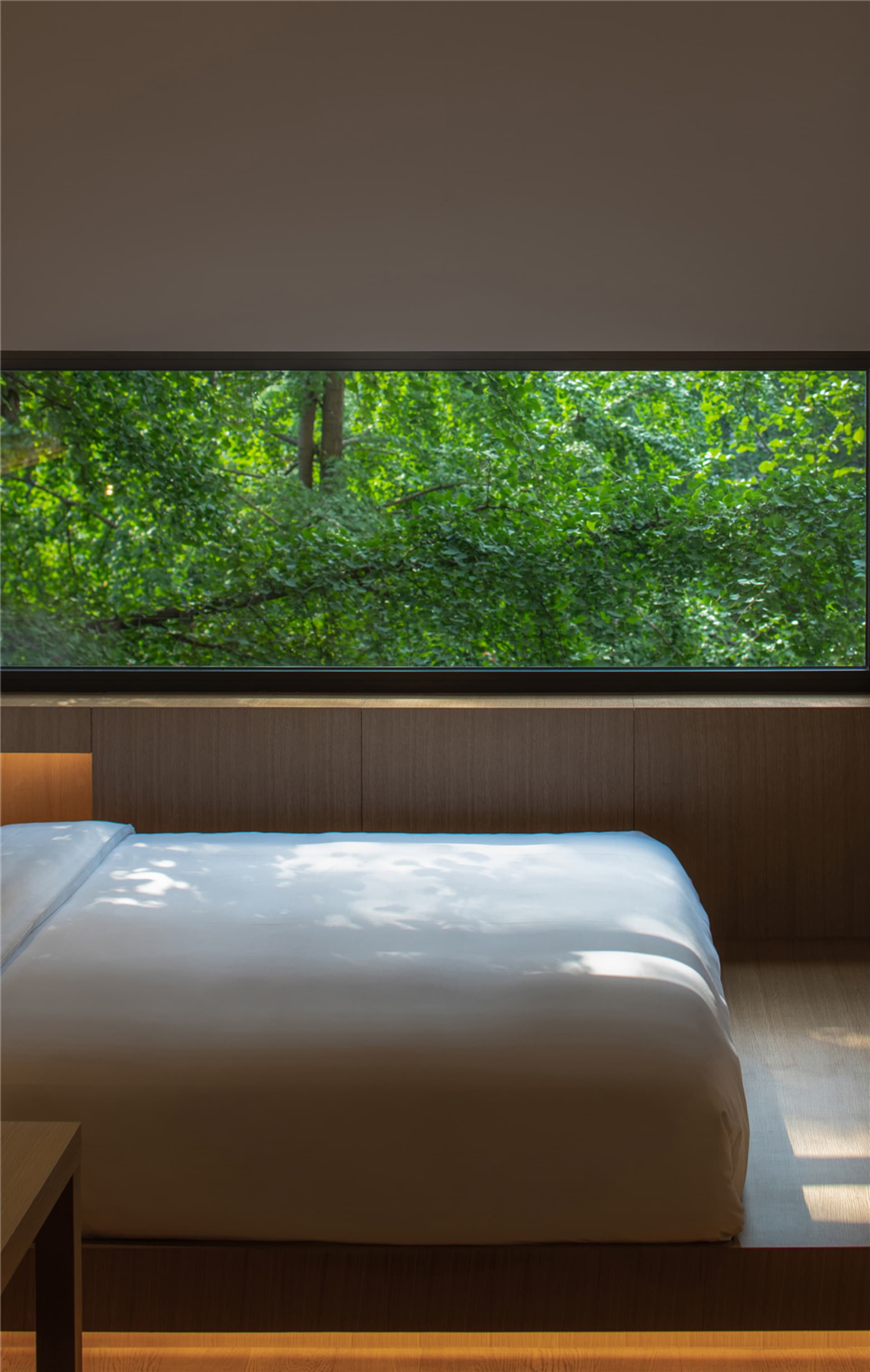 Modern bedroom with a zen-like atmosphere, featuring a bed surrounded by wooden walls and a large window with a view of lush